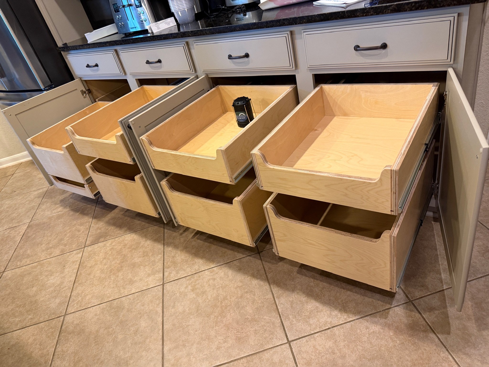 Pull out kitchen drawers open in a kitchen with white cabinets and a black countertop. Eight cabinets with two drawers each are fully extneded.