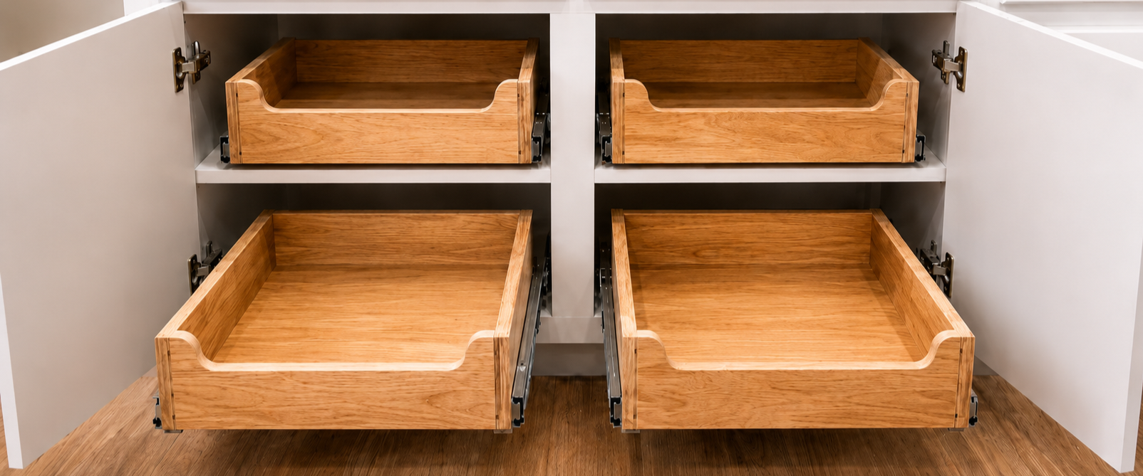 Open kitchen cabinet with four empty wooden drawers, two on the top and two on the bottom, all pulled out partially.