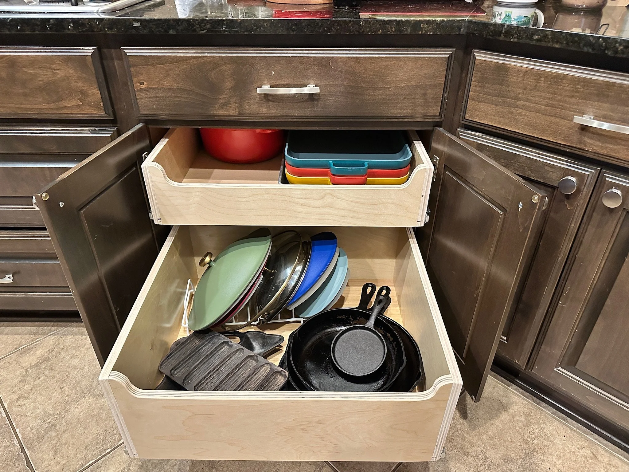 Open kitchen cabinet with stacked pots and pans, a red mixing bowl, and a dish rack with cutlery and utensils inside.