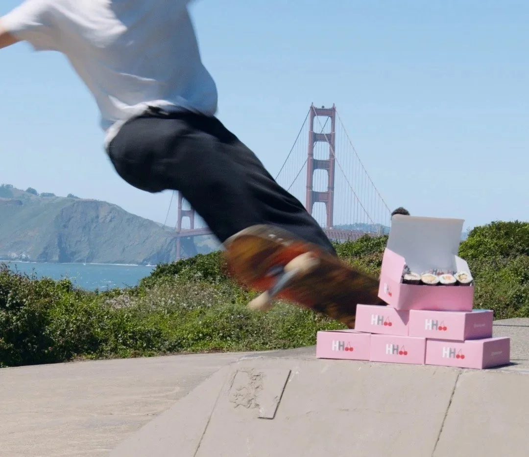 A skateboarder performing tricks near the Golden Gate Bridge with boxes of sushi on the ground