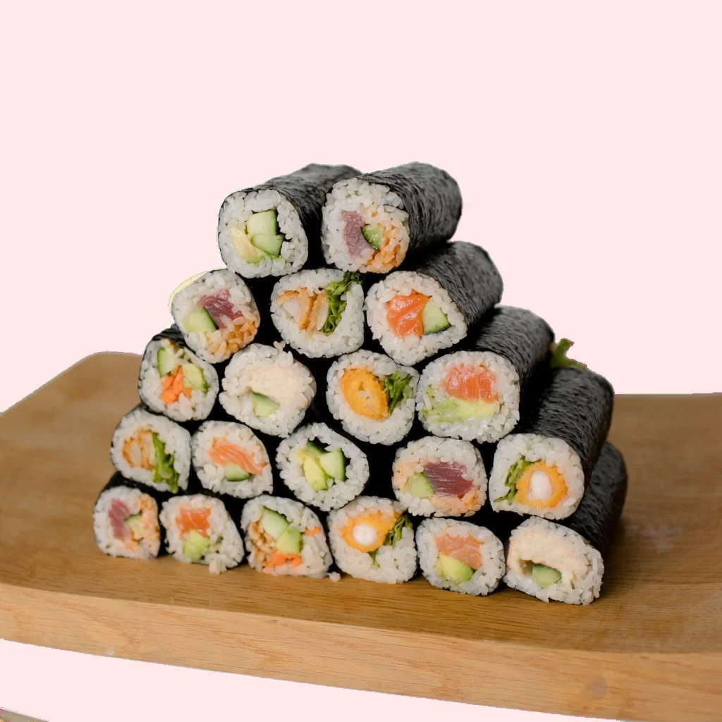 Sushi rolls stacked in a pyramid shape on a wooden cutting board against a pink background.