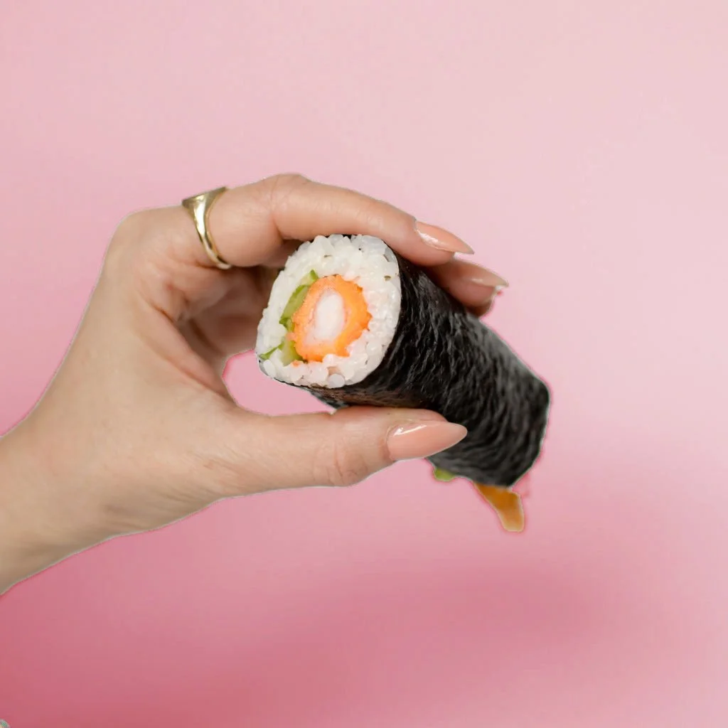 A hand holding a sushi roll against a pink background.