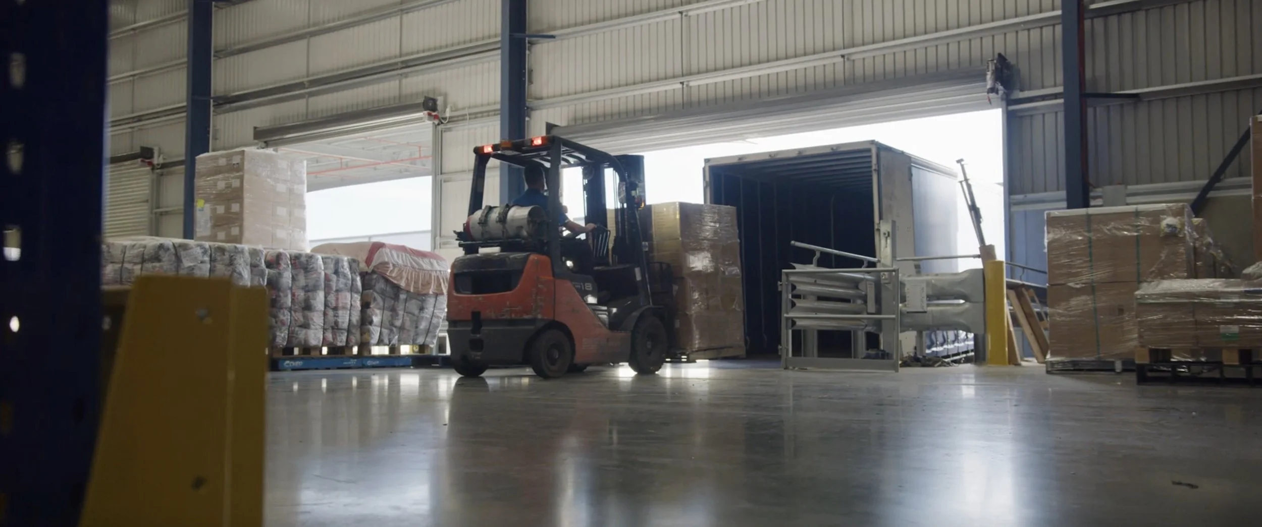 A forklift operator moving pallets of goods and brands for Amazon inside a large warehouse.