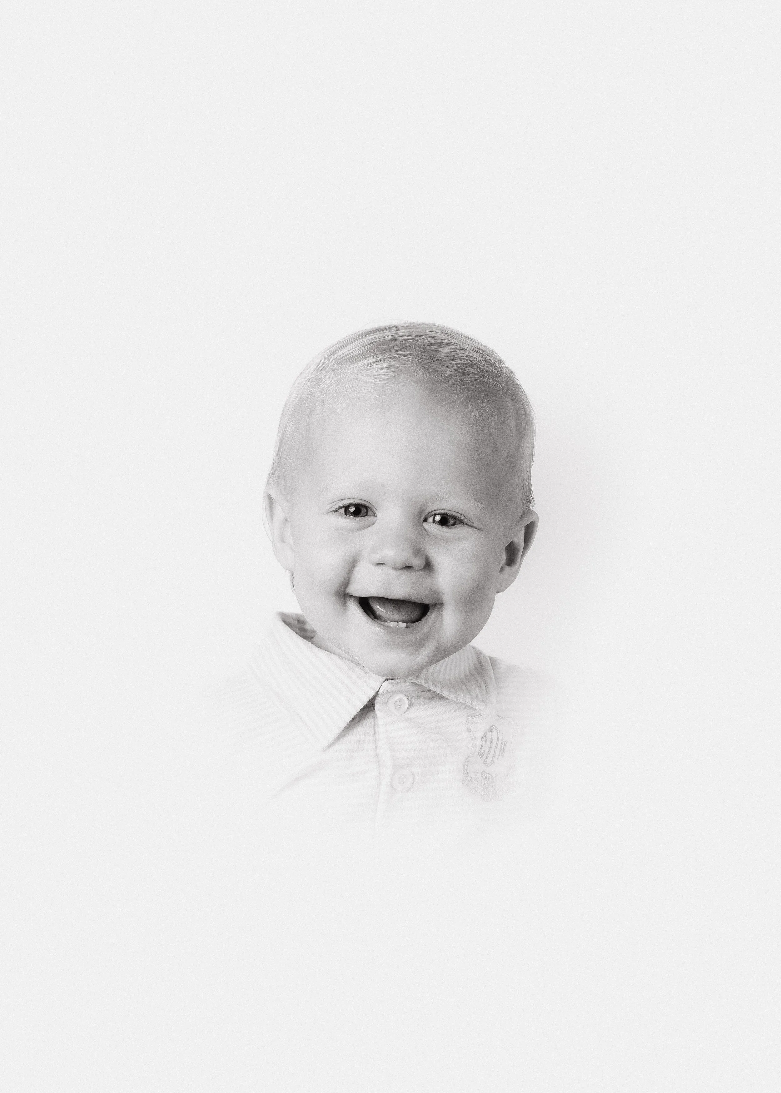 Black and white photo of a young boy smiling and showing his tongue, wearing a collared shirt.