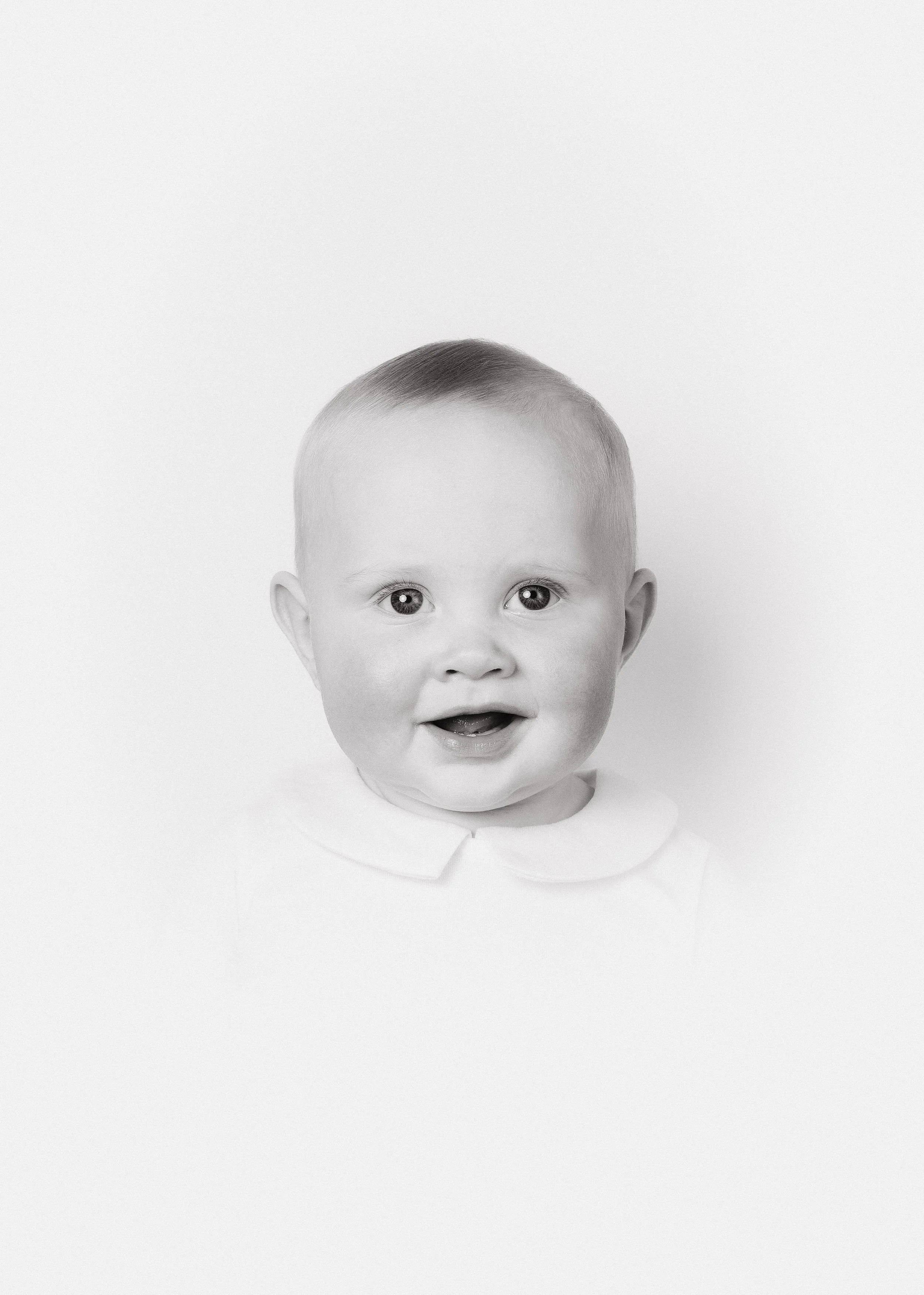 Black and white photo of a smiling young child with short hair, wearing a collared shirt, against a plain background.