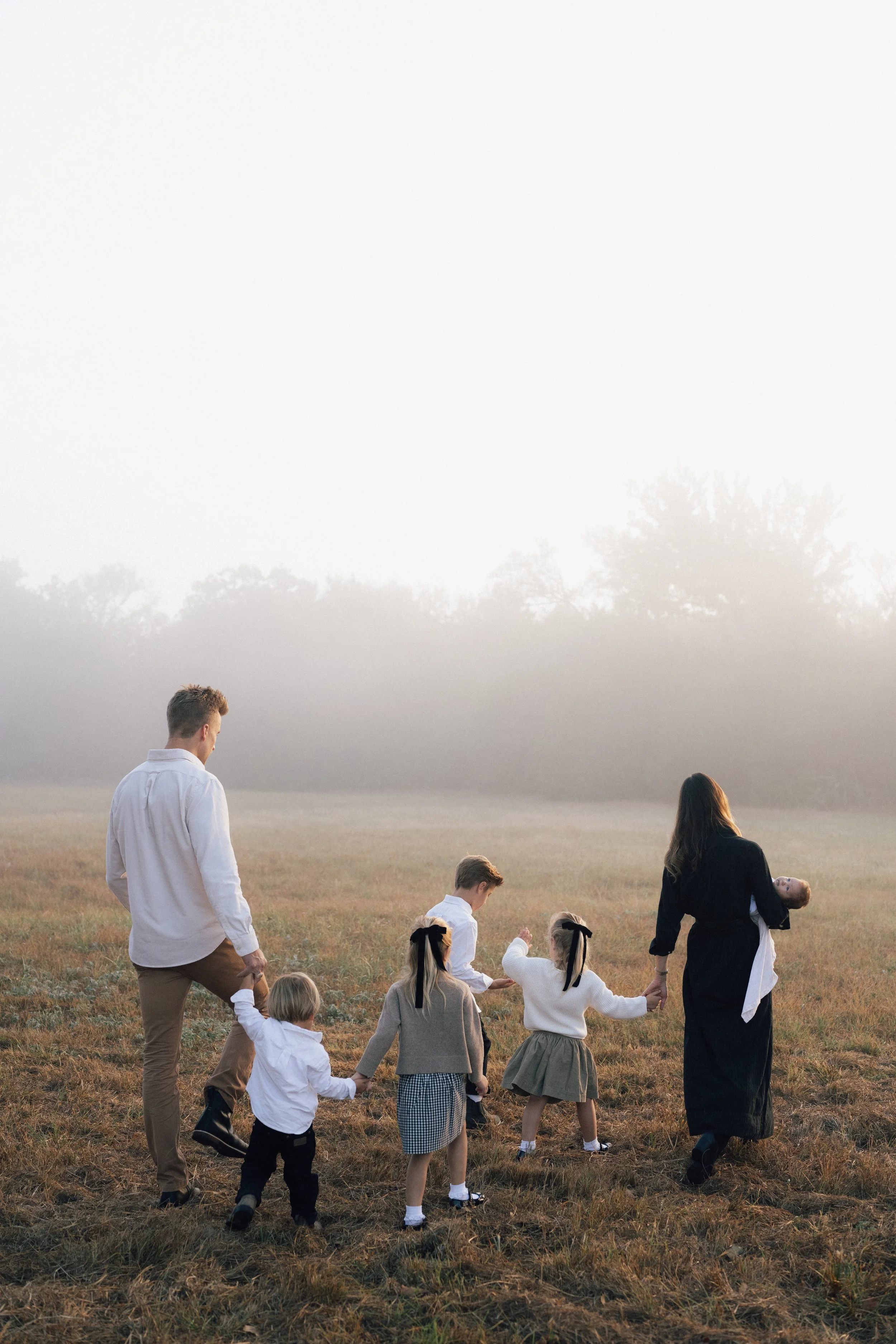 A family walking and playing together in a grassy field during sunrise or sunset.