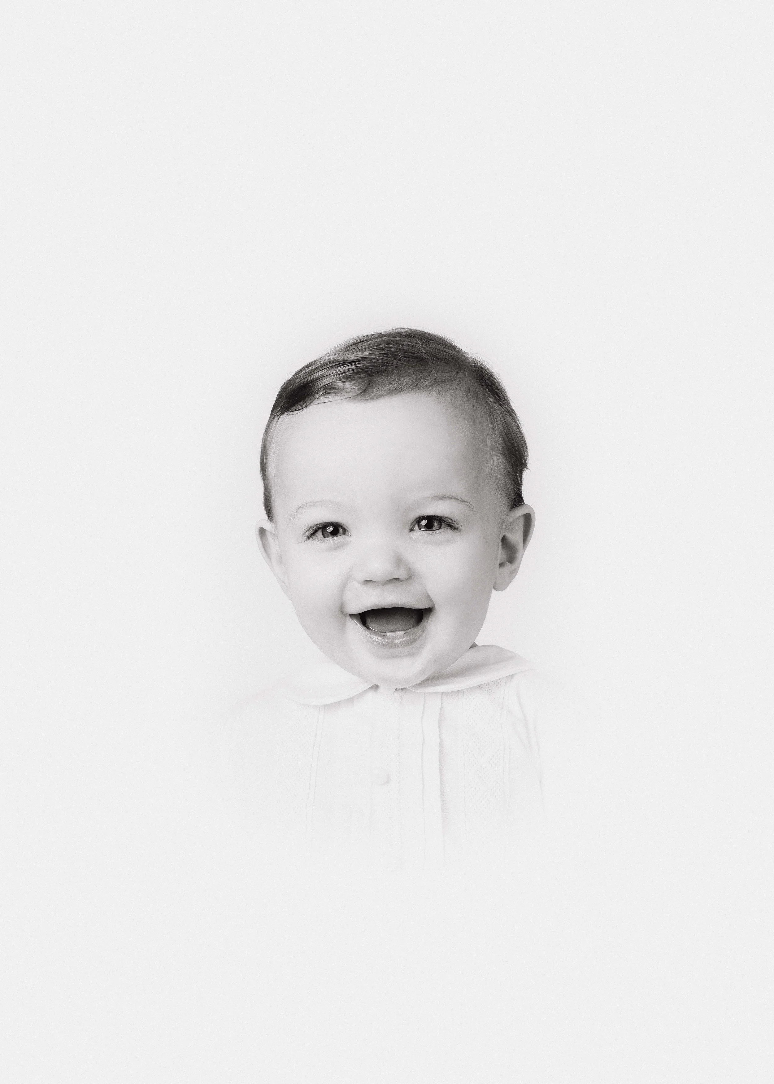Black and white photo of a smiling young child with short hair, wearing a white shirt, with a joyful expression on their face.
