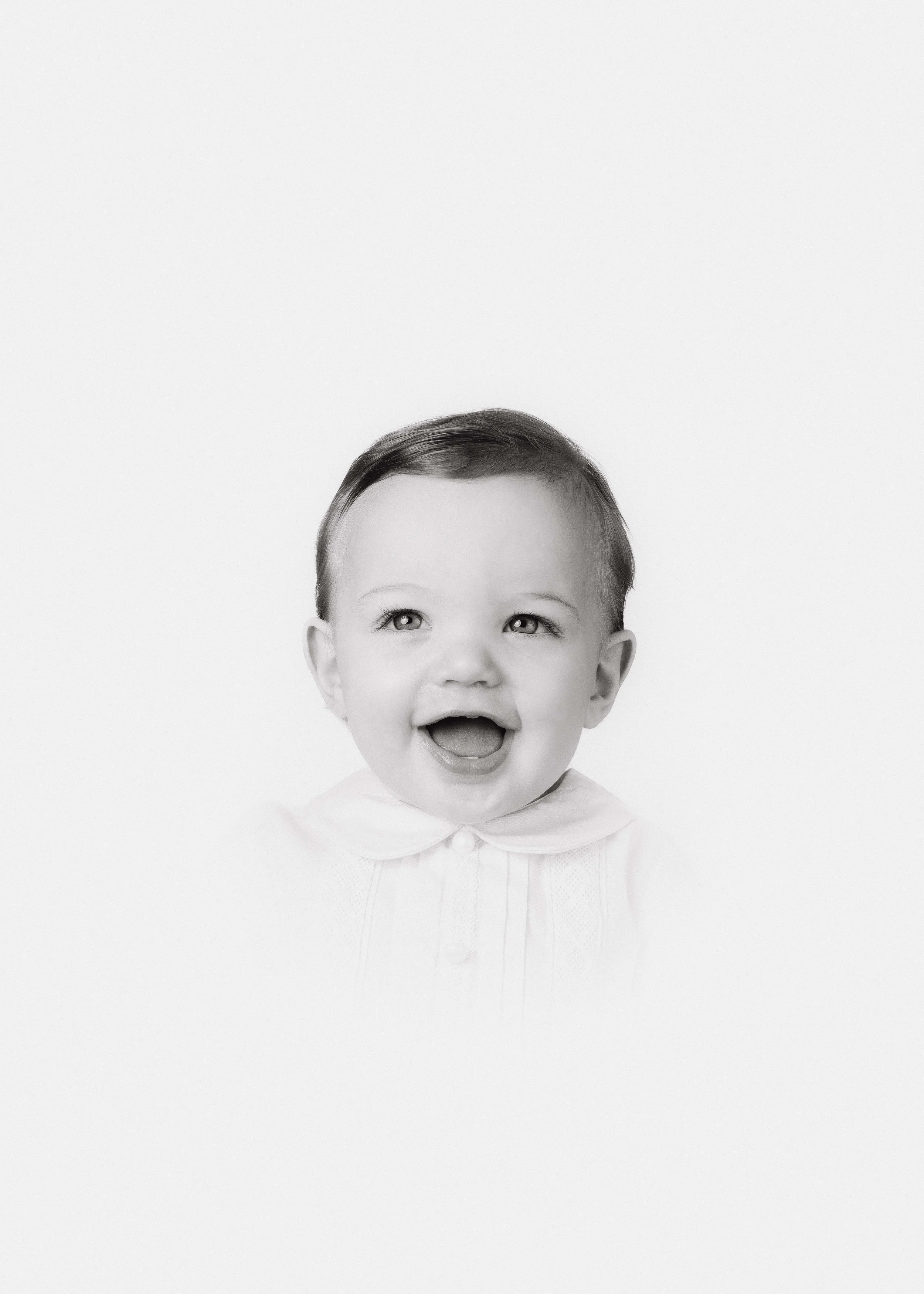 Black and white photo of a smiling toddler with short dark hair, wearing a collared shirt, against a plain white background.