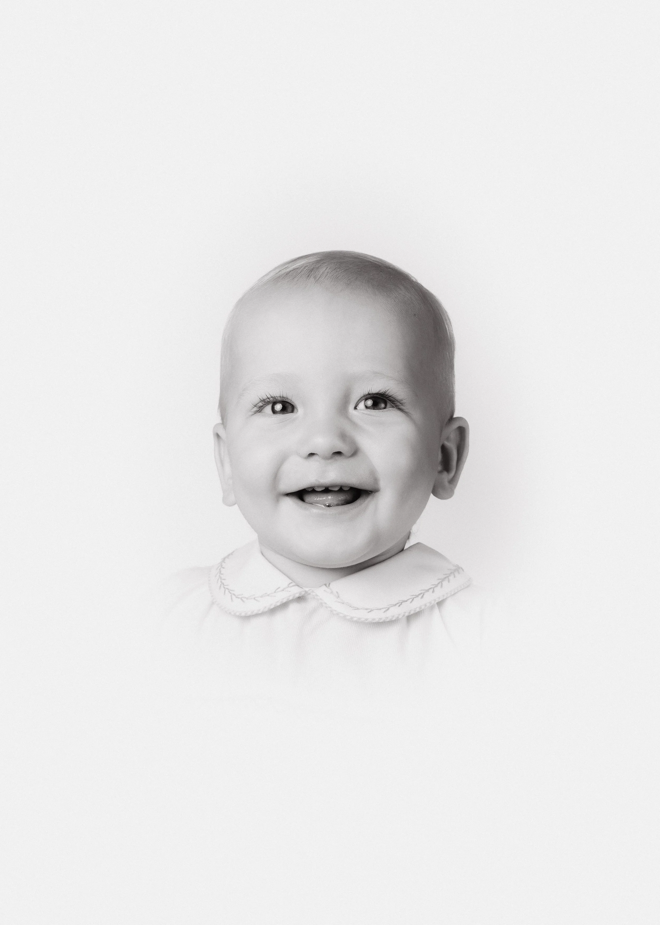 Black and white photo of a smiling young boy with short hair, wearing a collared shirt, against a plain background.