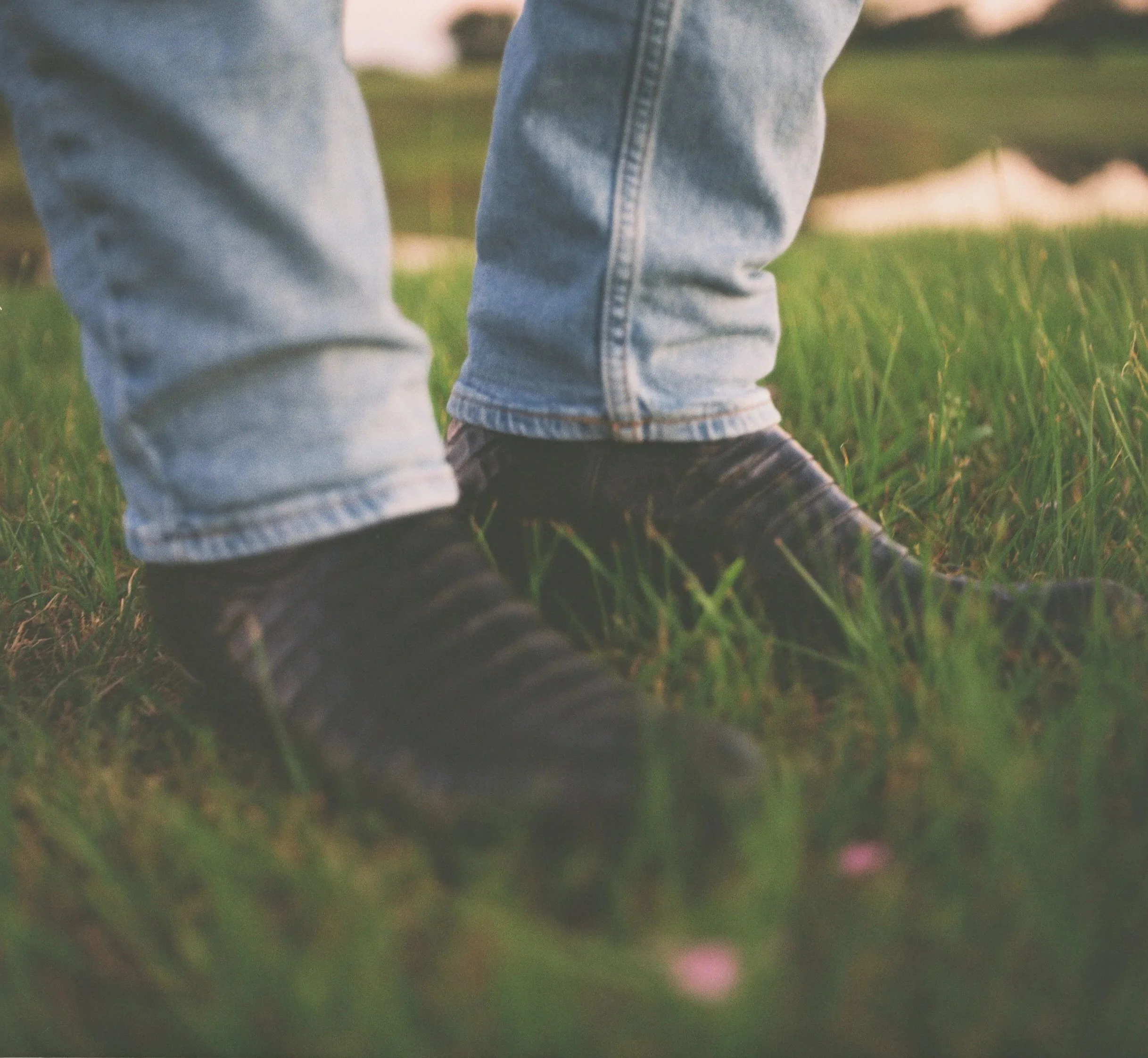 Close-up of a person wearing light blue jeans walking on grass.