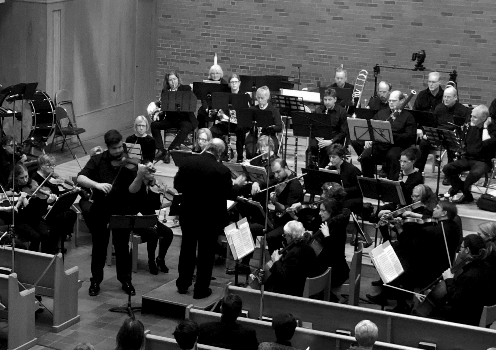 An orchestra performing on stage in a concert hall with musicians playing string and wind instruments, directed by a conductor.