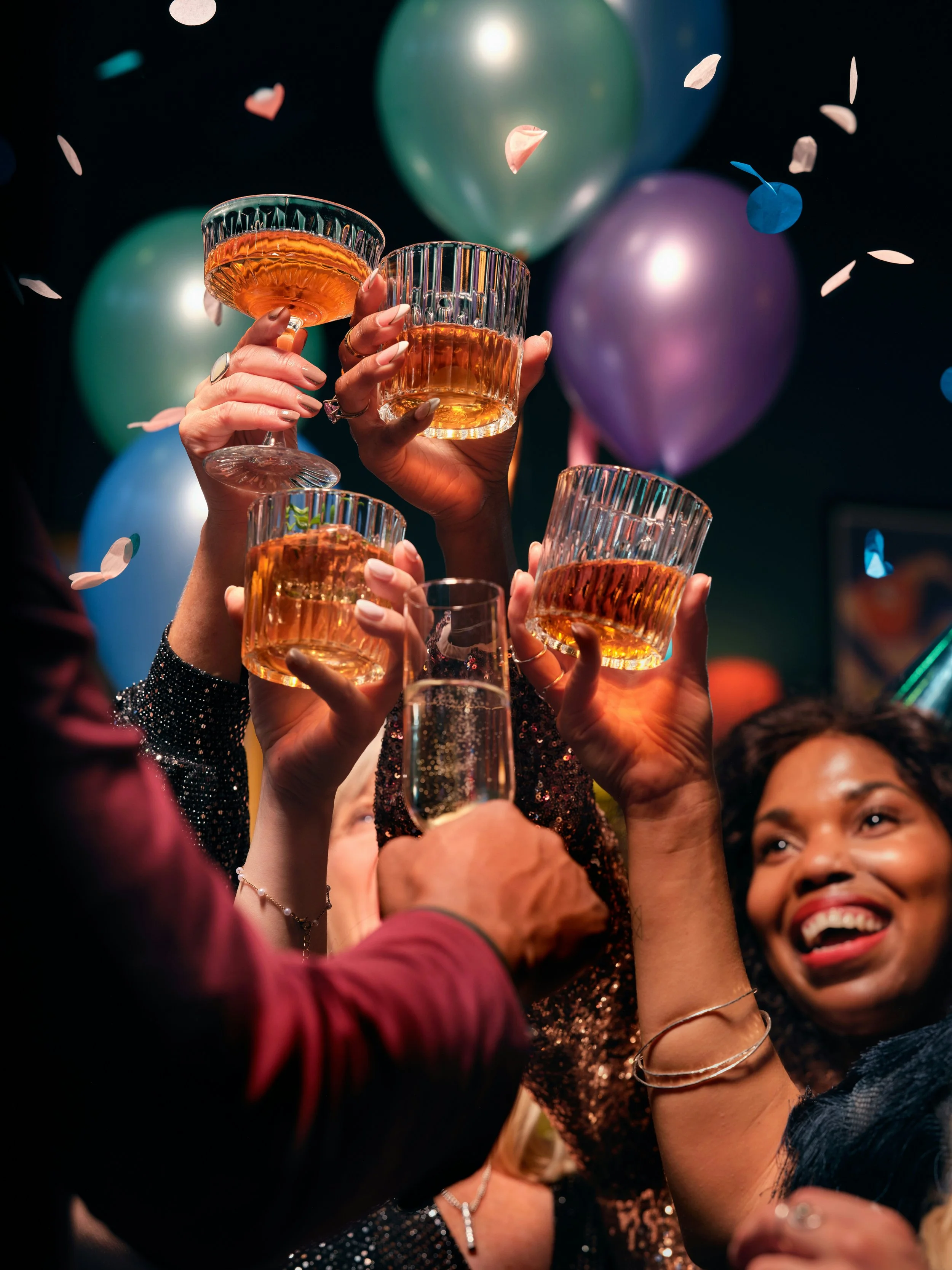 People celebrating at a party with balloons and drinks, raising glasses together with smiles.