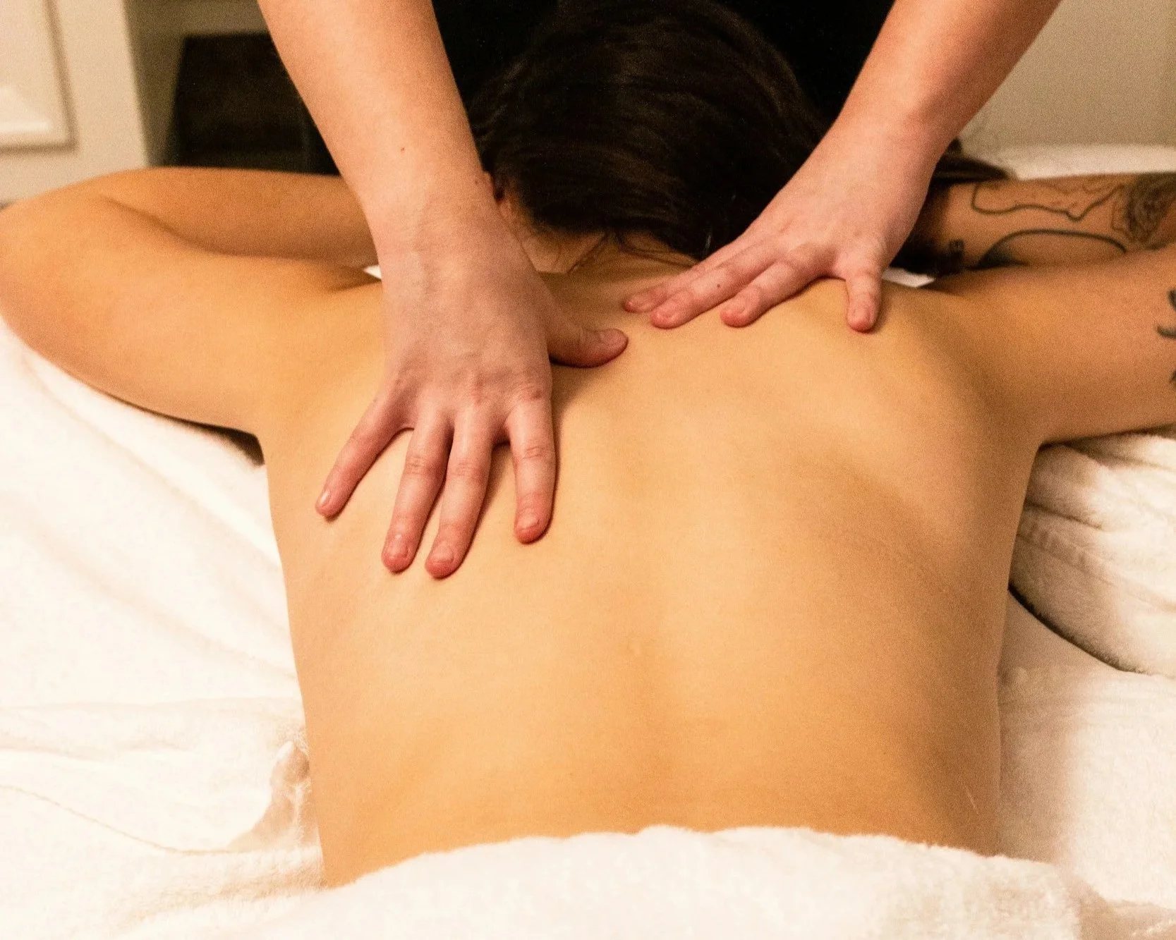 Eine Person erhält eine Rückenmassage im Liegen, während eine Masseurin ihre Hände auf den Rücken der Person legt.