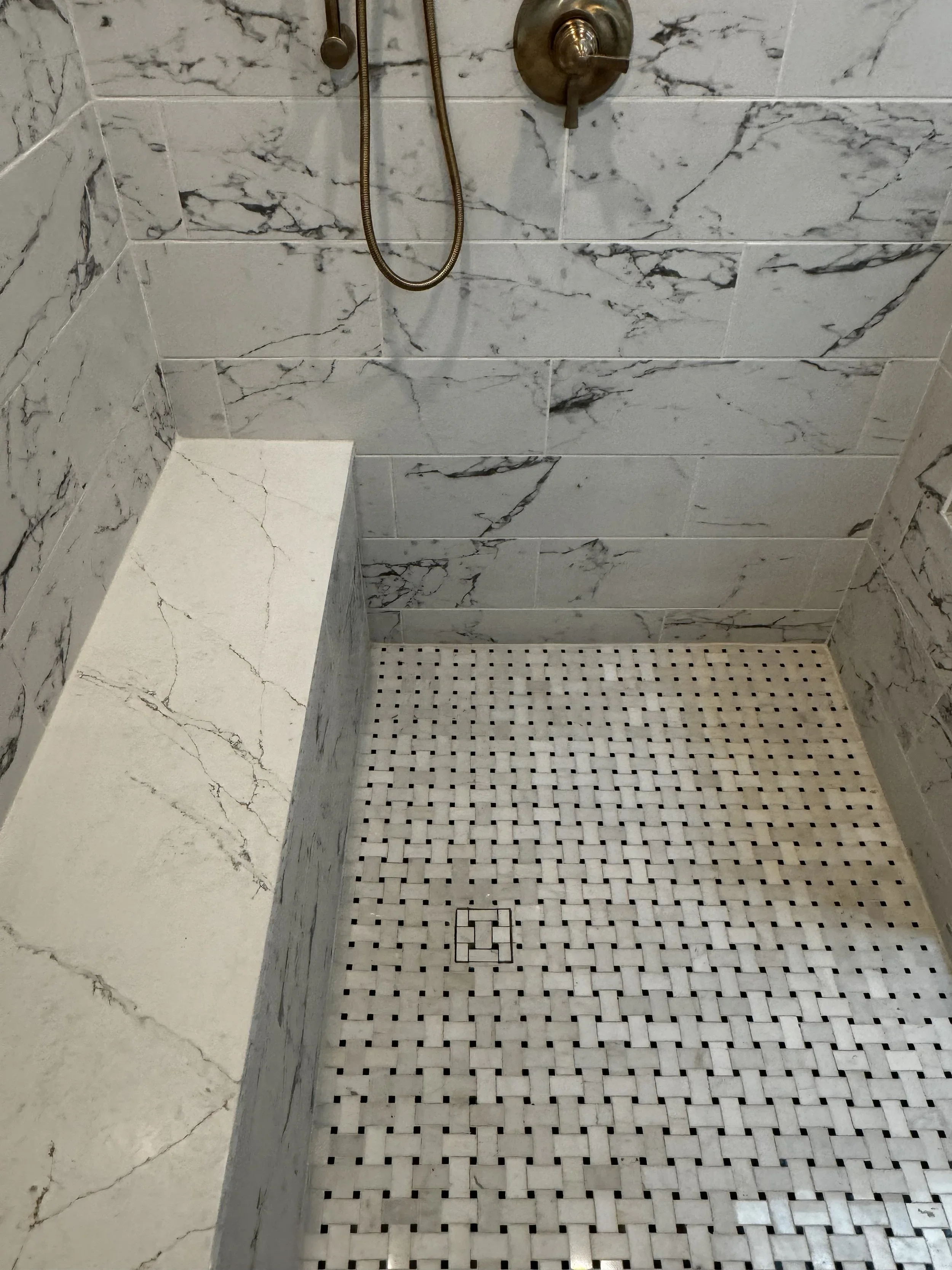 Marble-tiled shower with a built-in seat, a handheld shower head, and a mix of marble and mosaic tiles on the floor.