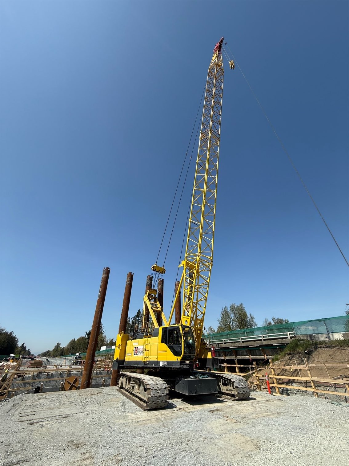 Yellow construction crane at a construction site with blue sky and trees in the background.