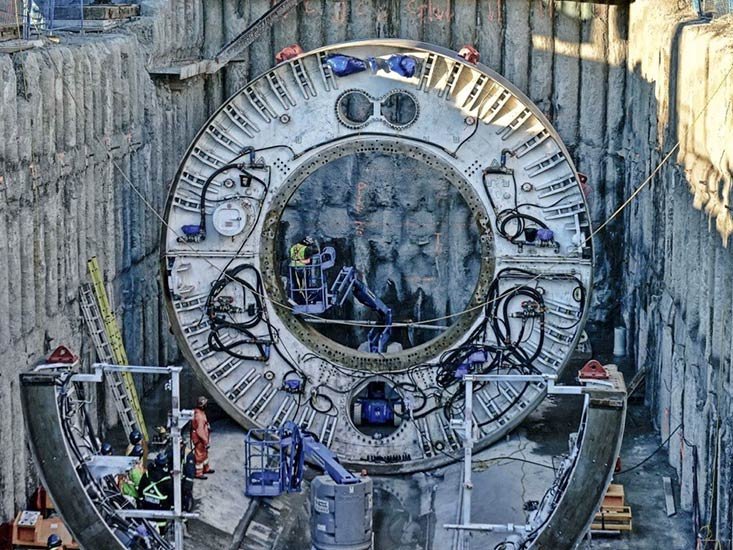 Construction workers working on a large clock face inside a deep excavation
