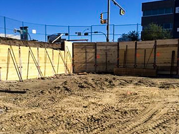 Construction site with wooden retaining walls, dirt ground, and a traffic light in the background.