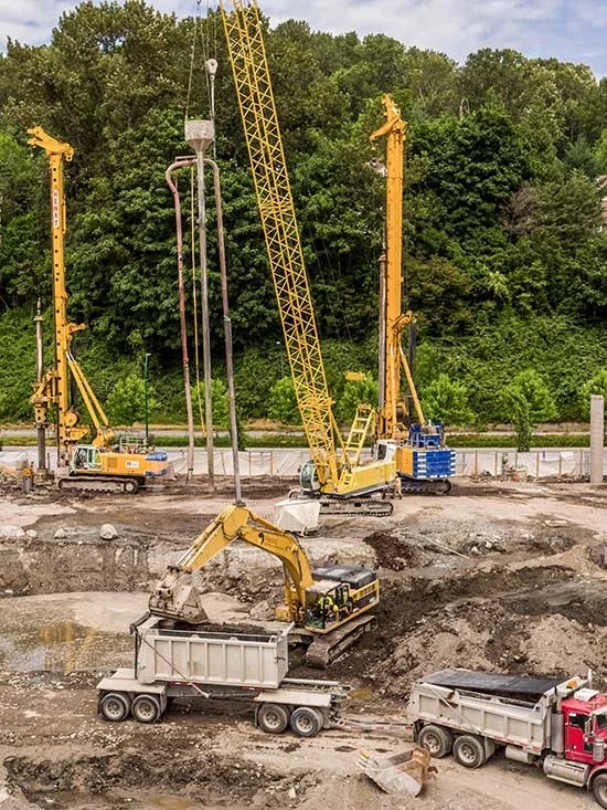 Construction site with yellow cranes and excavator, moving dirt and materials.