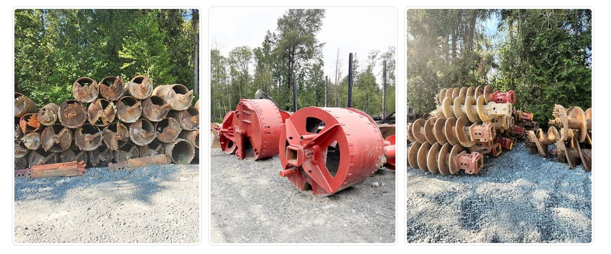Three sets of large, rusty, industrial equipment parts outdoors on gravel with trees in the background.