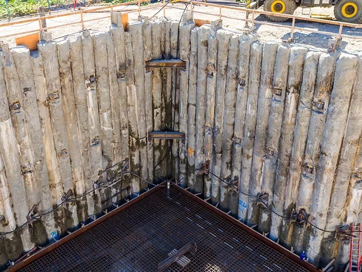 Construction site with vertical concrete retaining walls and a metal grid platform at the bottom.