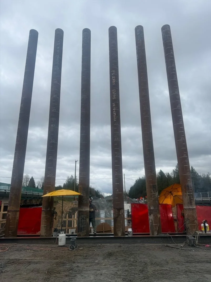 Large steel poles with measurement markings standing vertically at a construction site on a cloudy day.