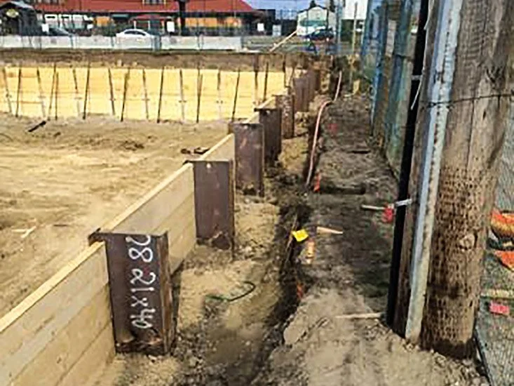 Construction site with vertical wooden and metal forms for concrete, dirt ground, and trees along the edge.