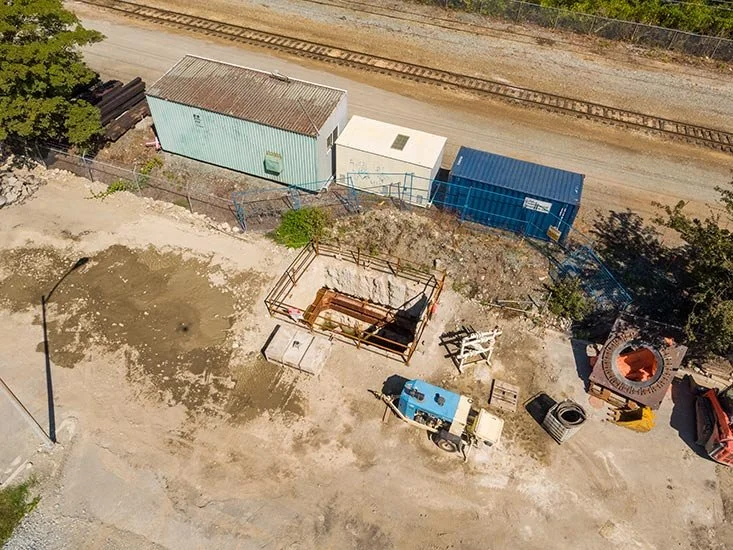 Construction site with three small storage buildings, construction tools, and equipment near a railway track.