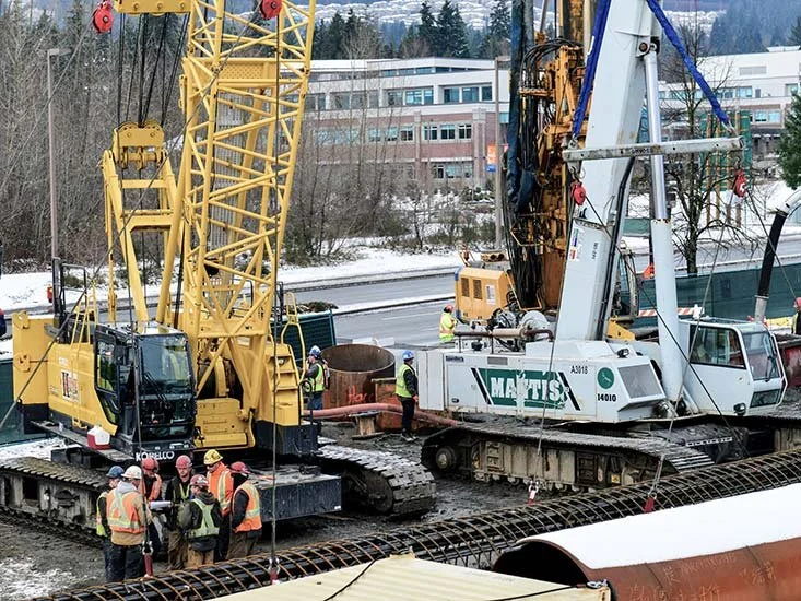 Construction workers operating heavy machinery on railroad tracks during daytime.