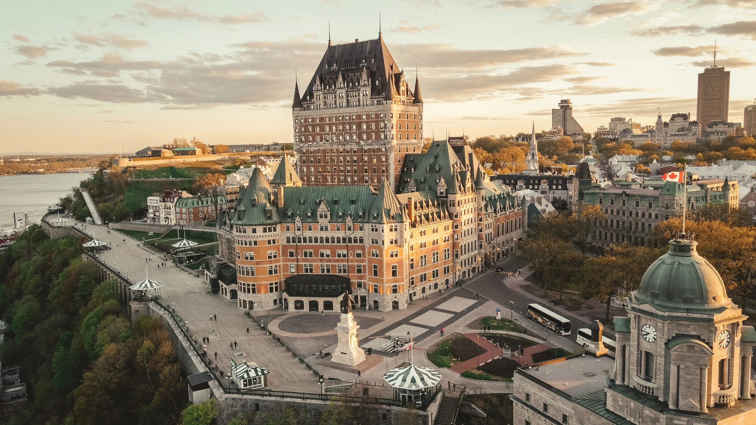 Vue panoramique du château Frontenac à Québec, avec ses toits en bois verts, la cathédrale et un fleuve, sous un ciel partiellement nuageux au crépuscule.