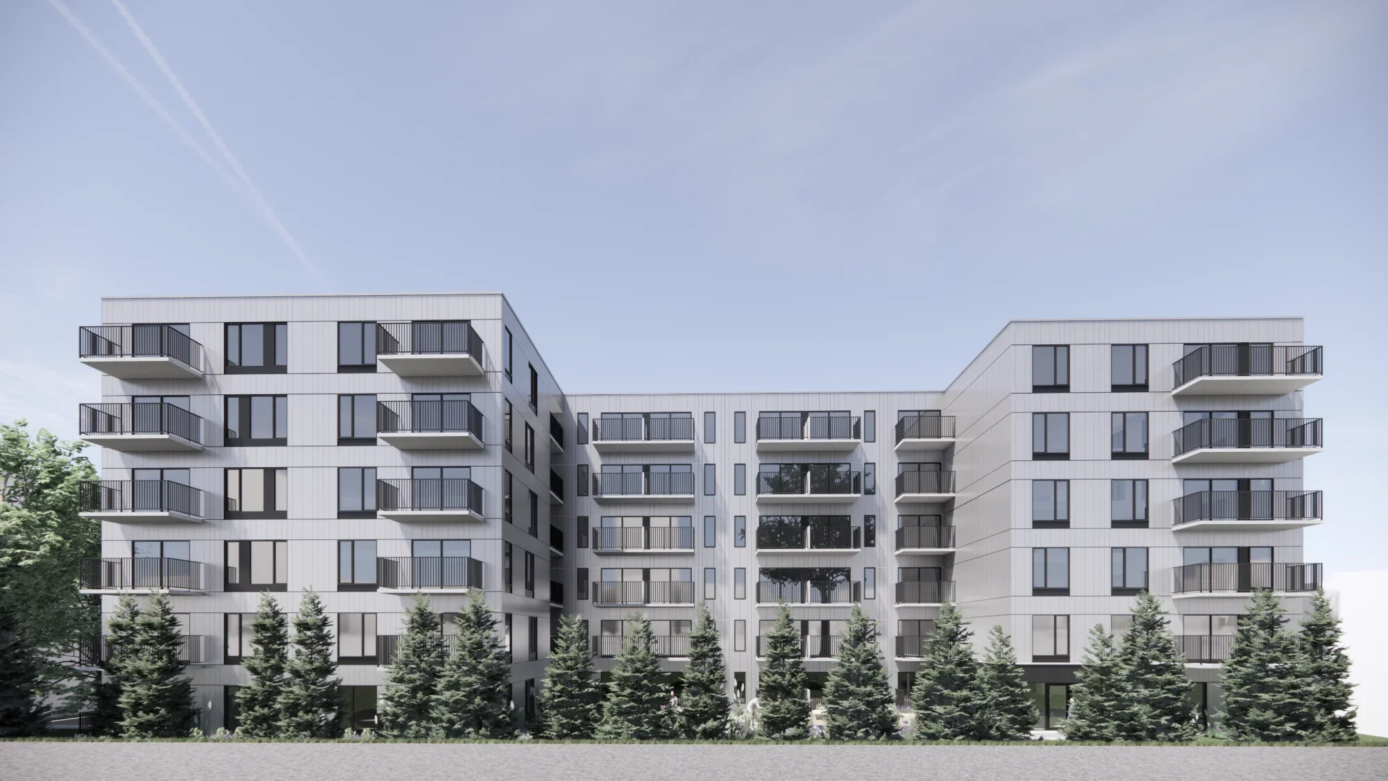Un bâtiment résidentiel moderne avec plusieurs étages, de grandes fenêtres et des balcons en métal noir, avec des arbres verts au premier plan et un ciel clair en arrière-plan.