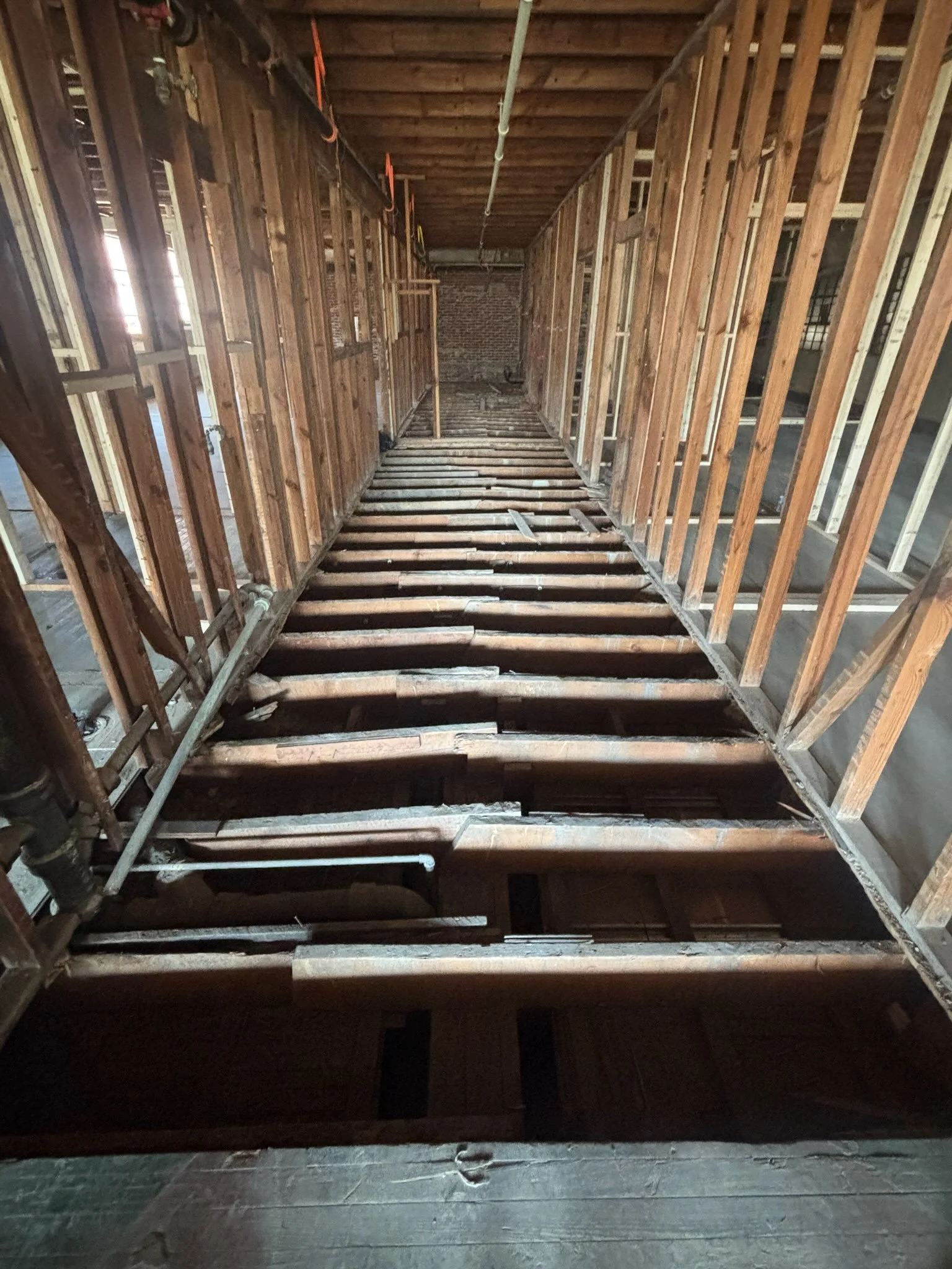 View of a house interior with exposed wooden framing, insulation, and pipes, during construction or renovation.