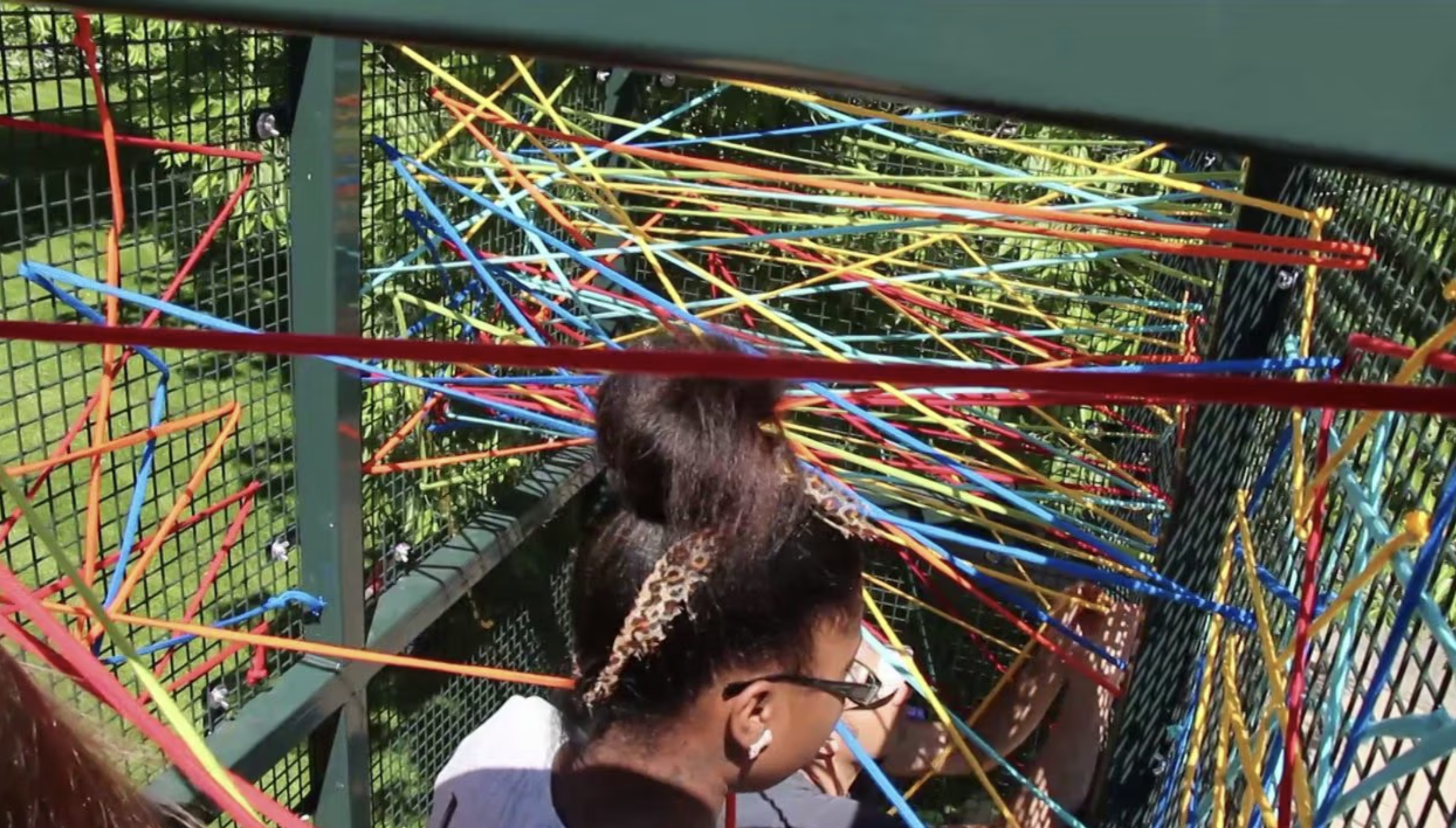 A young person stands inside artist Randy Walker's sculpture made of interwoven colorful cords