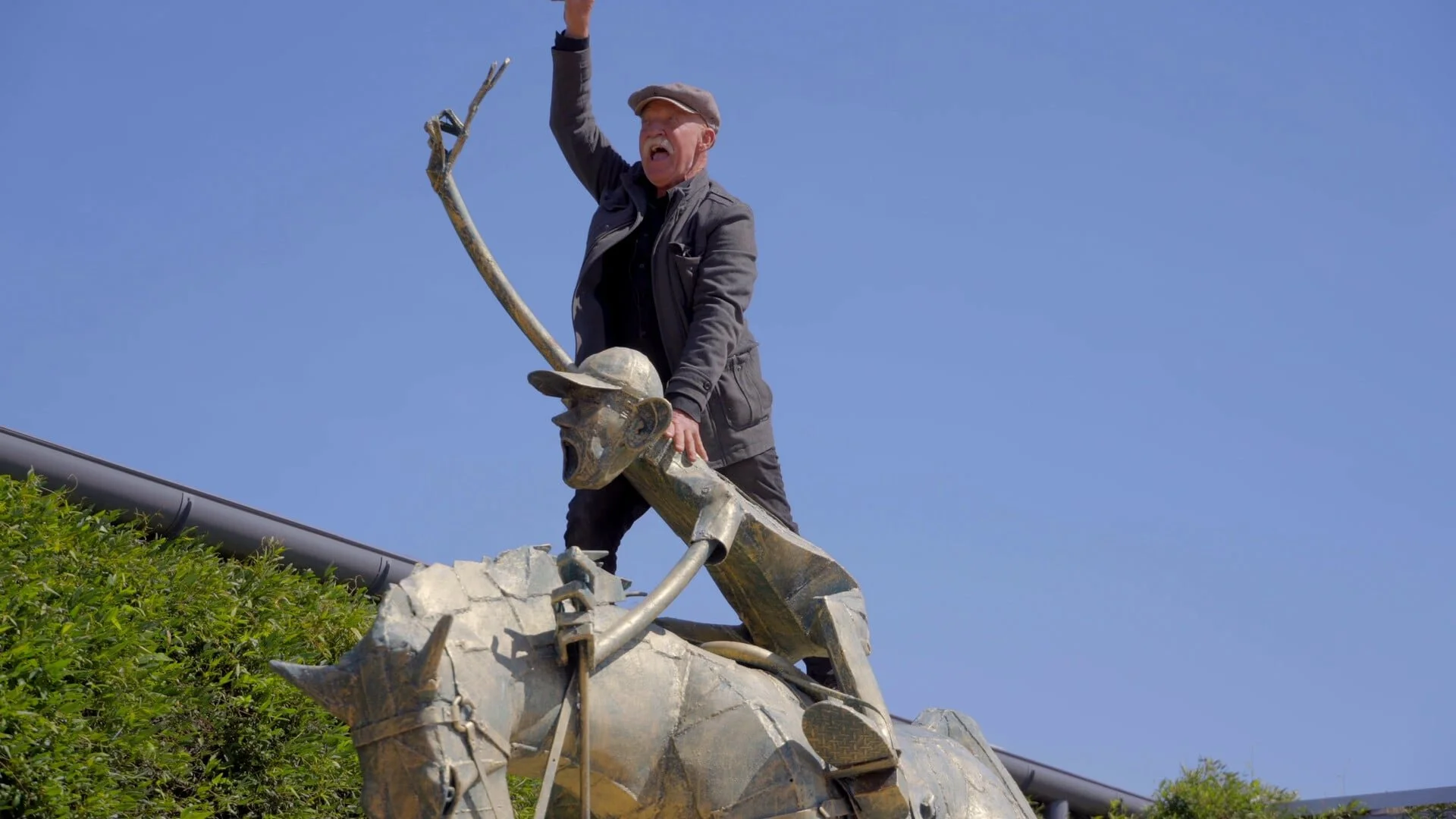 Artist Len Zuks stands atop his sculpture with one arm raised in the air