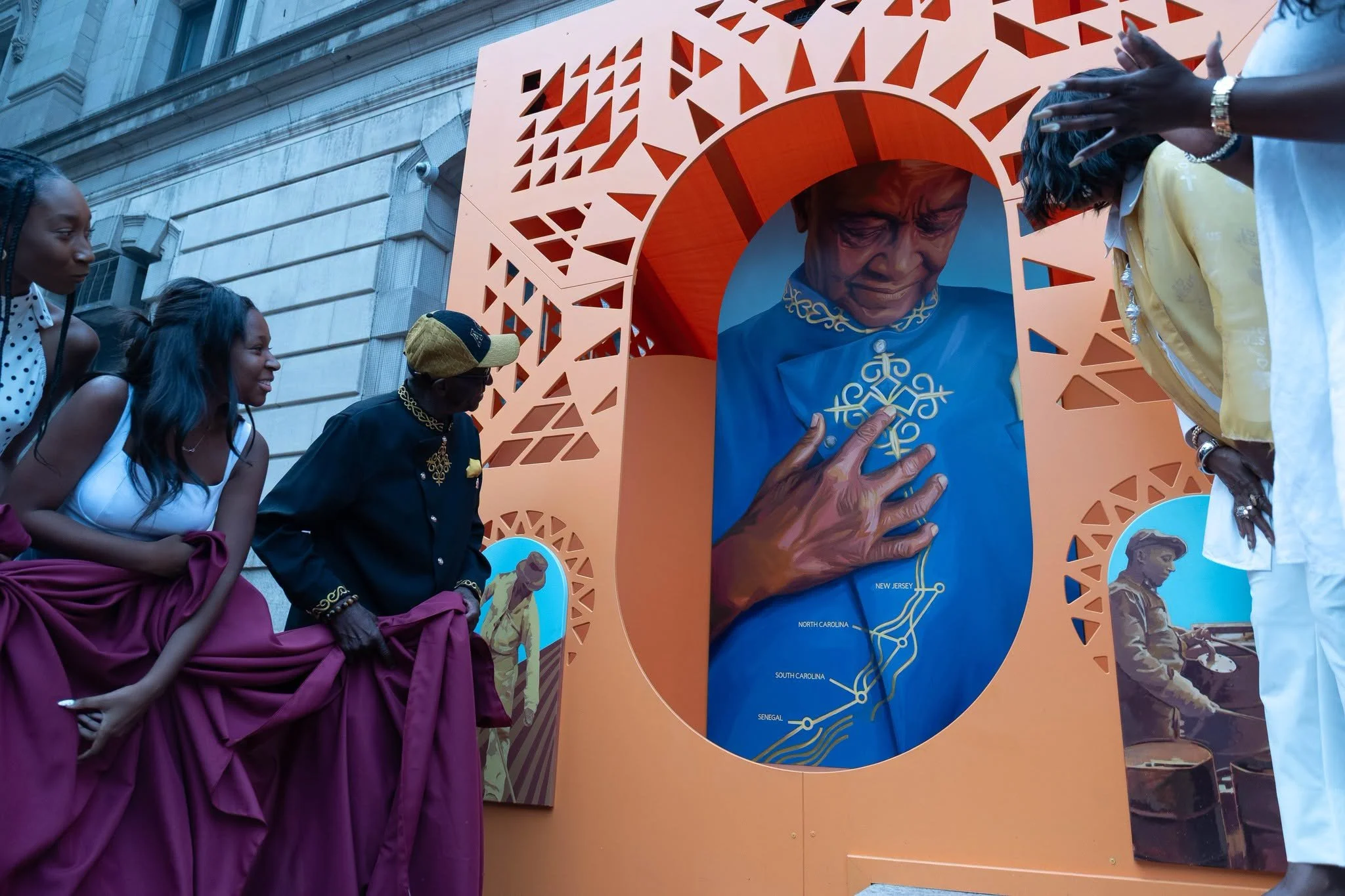 Three audience members stand next to a large orange sculpture framing a mural