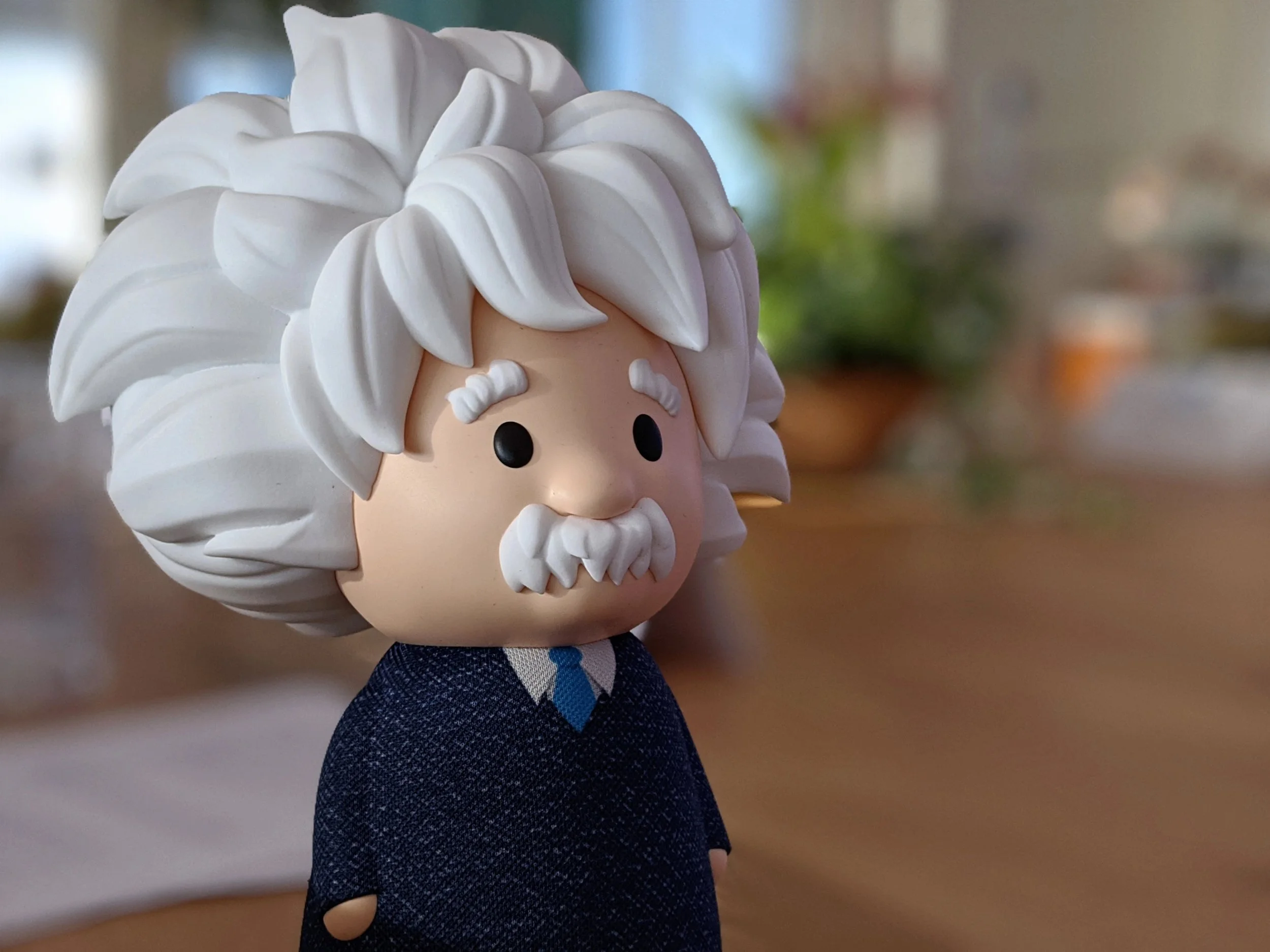 A stylized figurine of a bearded man with wild white hair, wearing a blue suit with a checkered pattern and a blue tie.