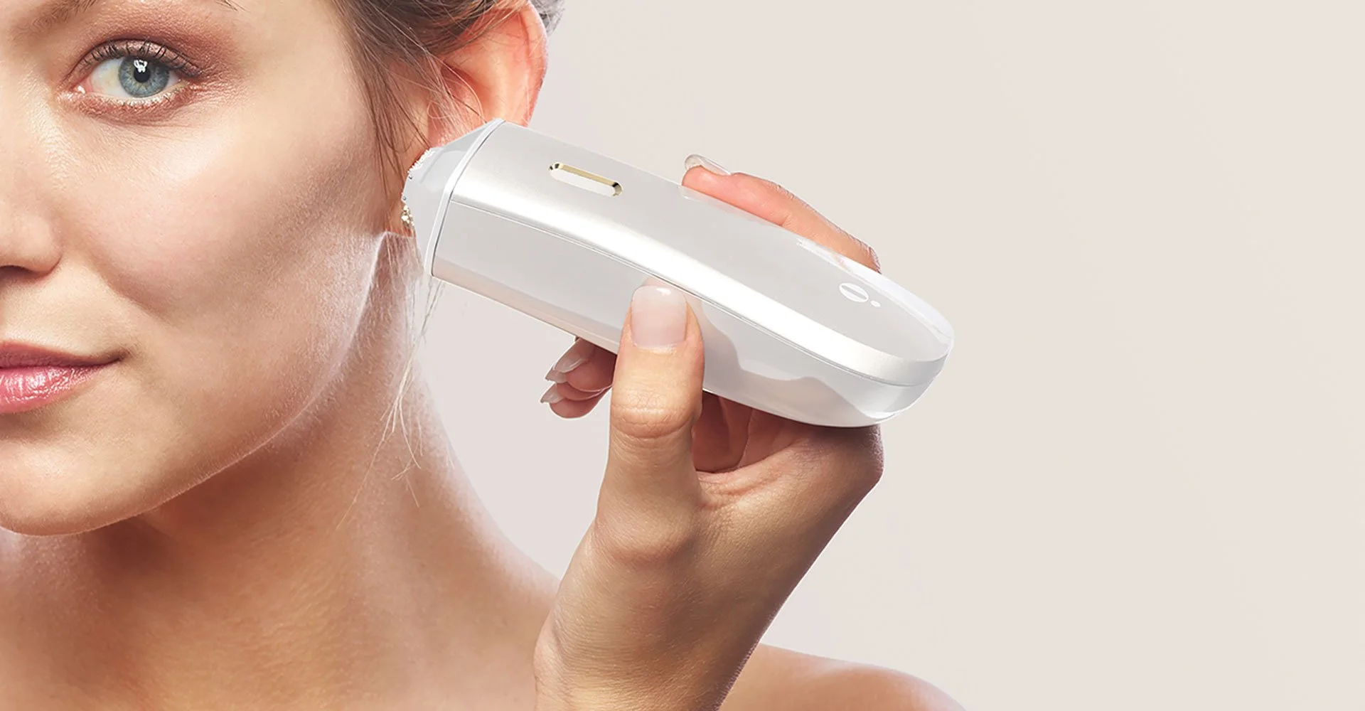 A woman holding a handheld skincare device to her face, with part of her face and neck visible against a plain background.