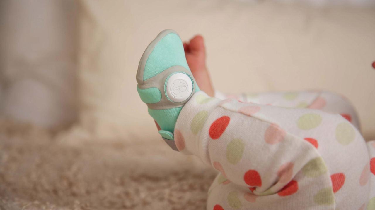 Child wearing pastel polka dot pajamas and turquoise-and-gray shoes lying on a carpeted floor.