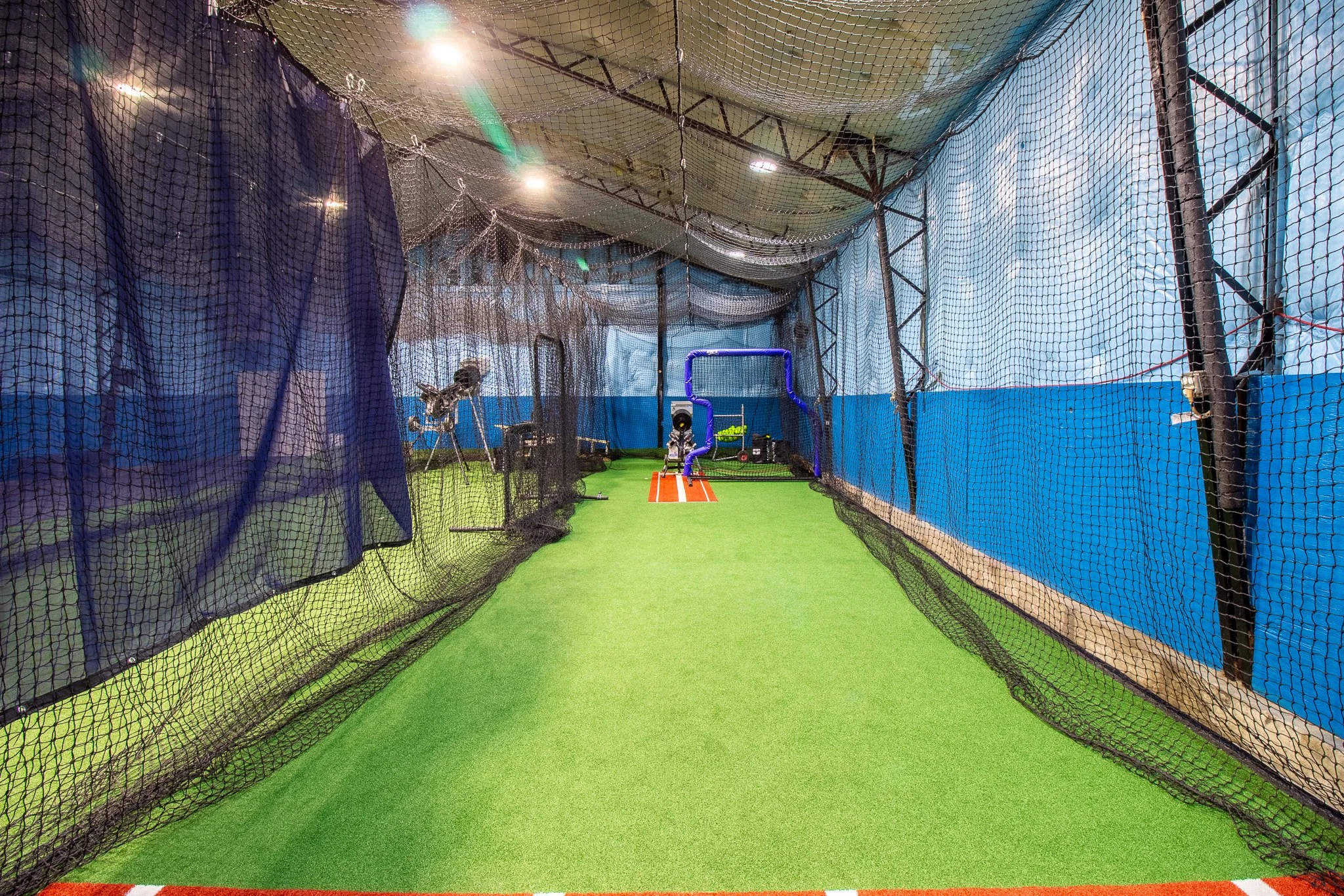 Indoor batting cage with nets, batting tee, and sports equipment on artificial turf.