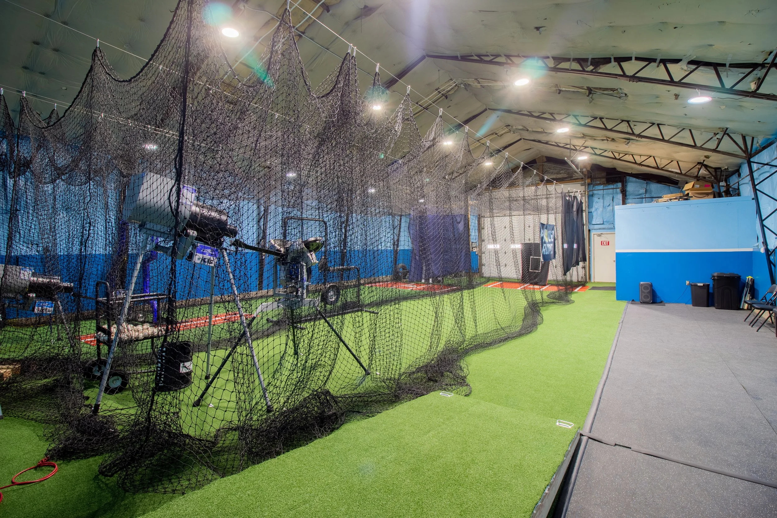 Indoor golf practice area with artificial turf, golf nets, and golf equipment, illuminated by ceiling lights.