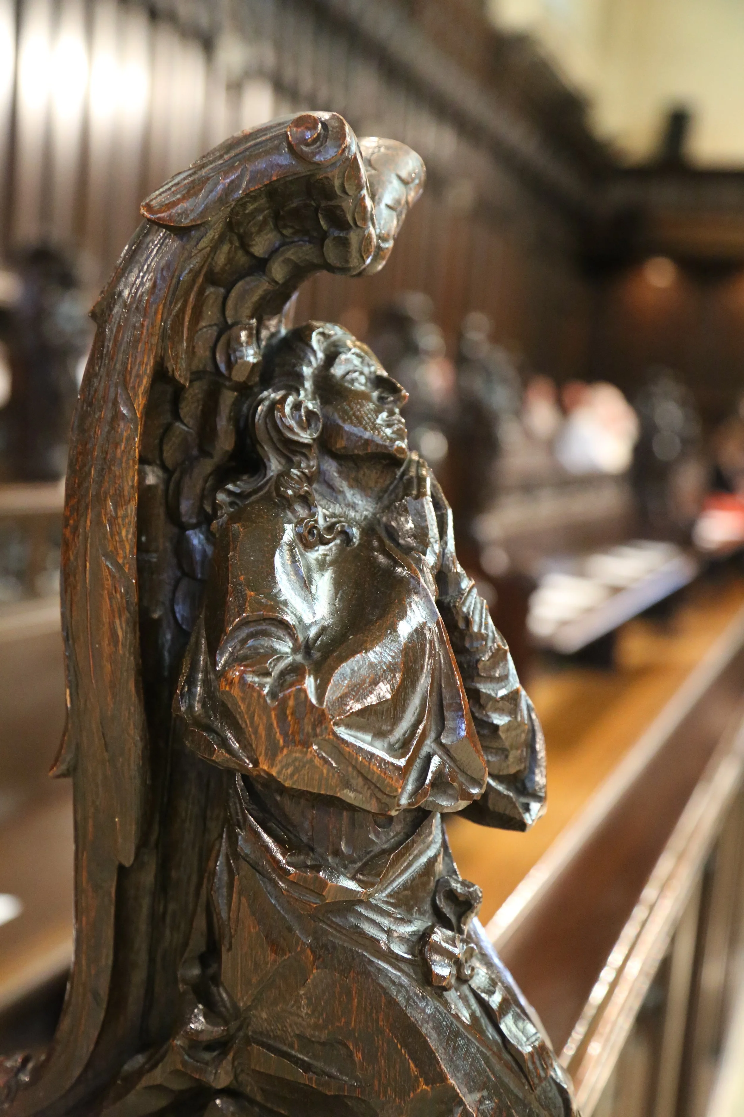Close-up of a dark wood carved decorative element featuring a profile of a woman with long hair, adorned with a round earring, surrounded by intricate floral and leaf motifs.