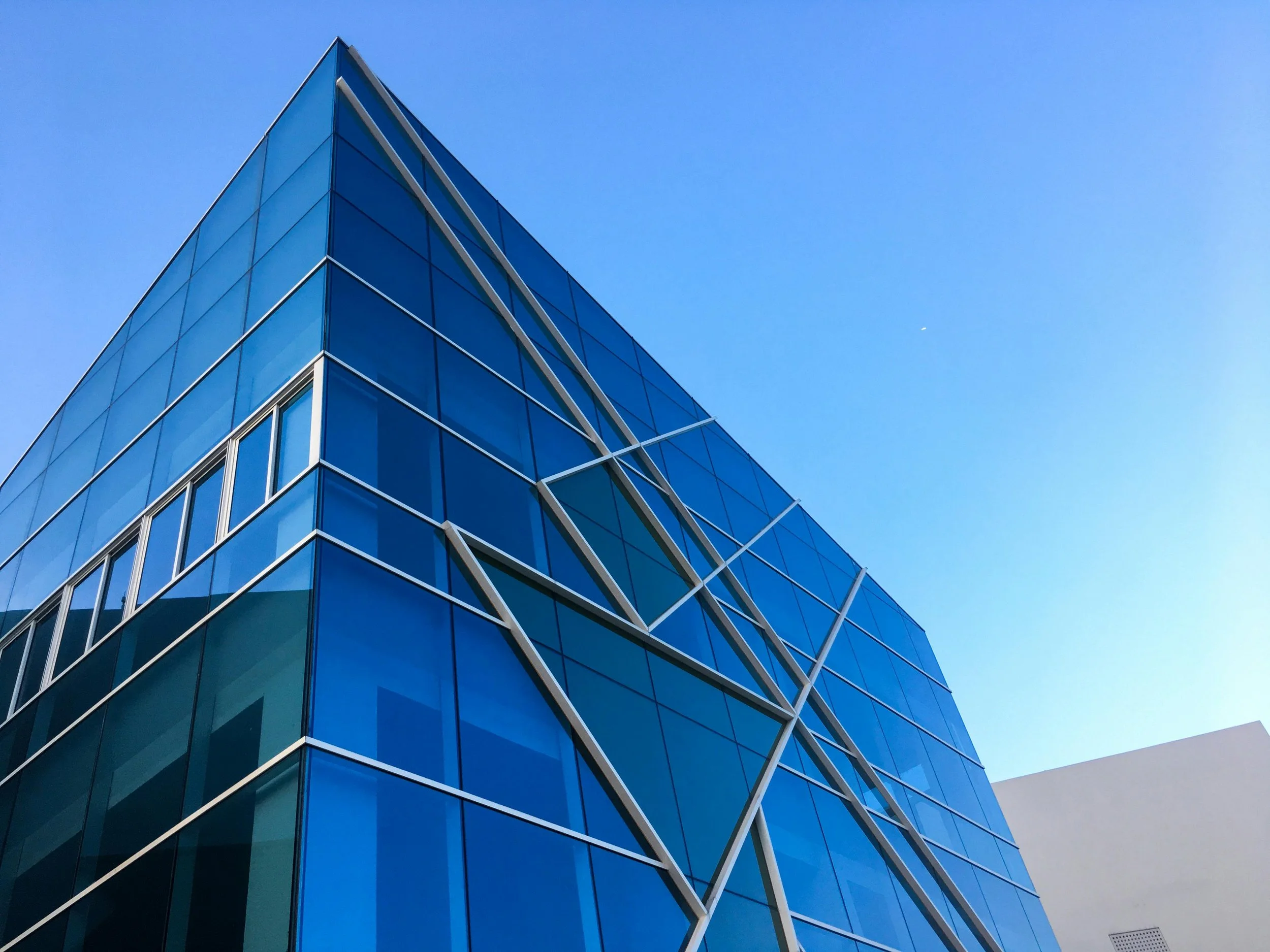 Modern glass building with sharp corner and reflective blue windows against a clear blue sky.