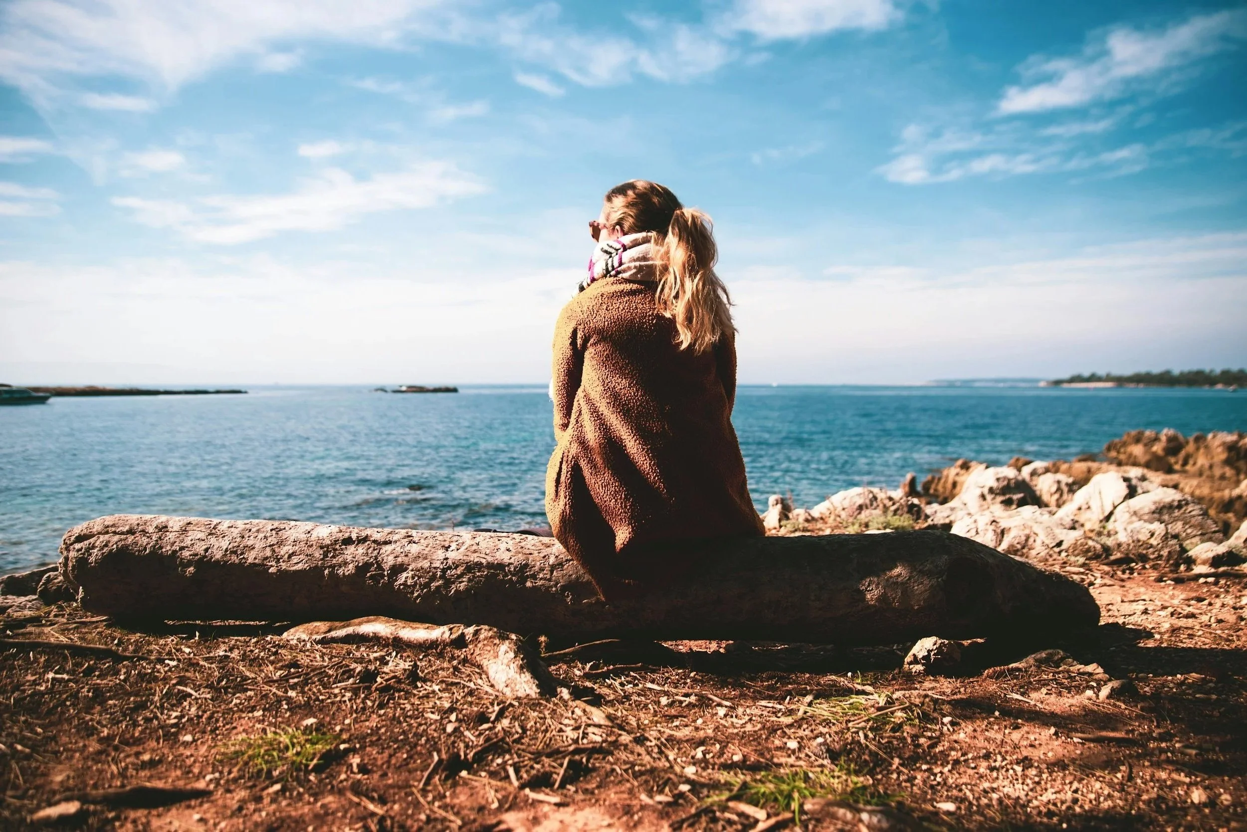 Two individuals sitting together by the shoreline representing support, healing, and recovery from trauma.