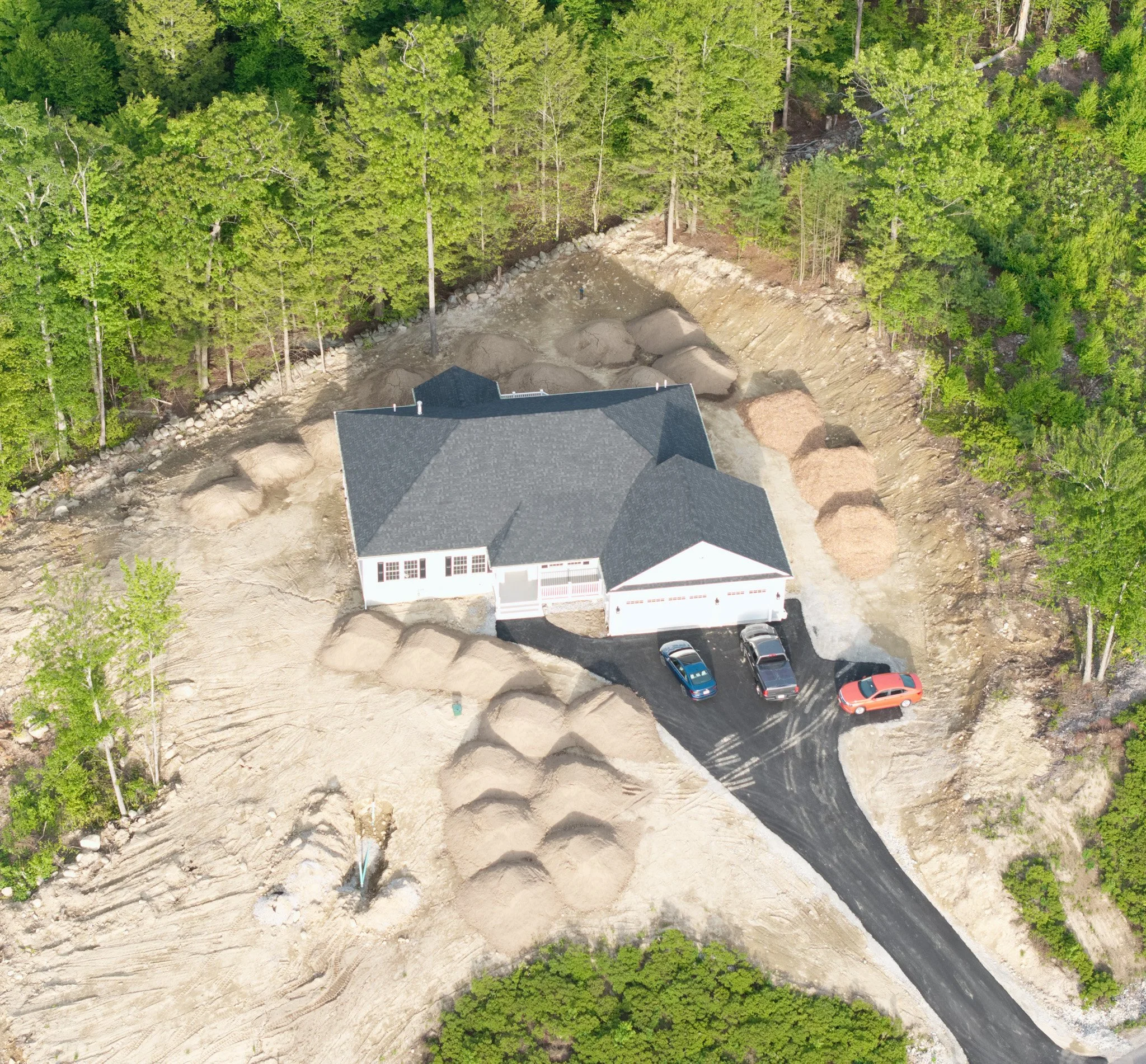 Aerial view of a house surrounded by trees and a construction or excavation site with dirt mounds and disturbed ground.