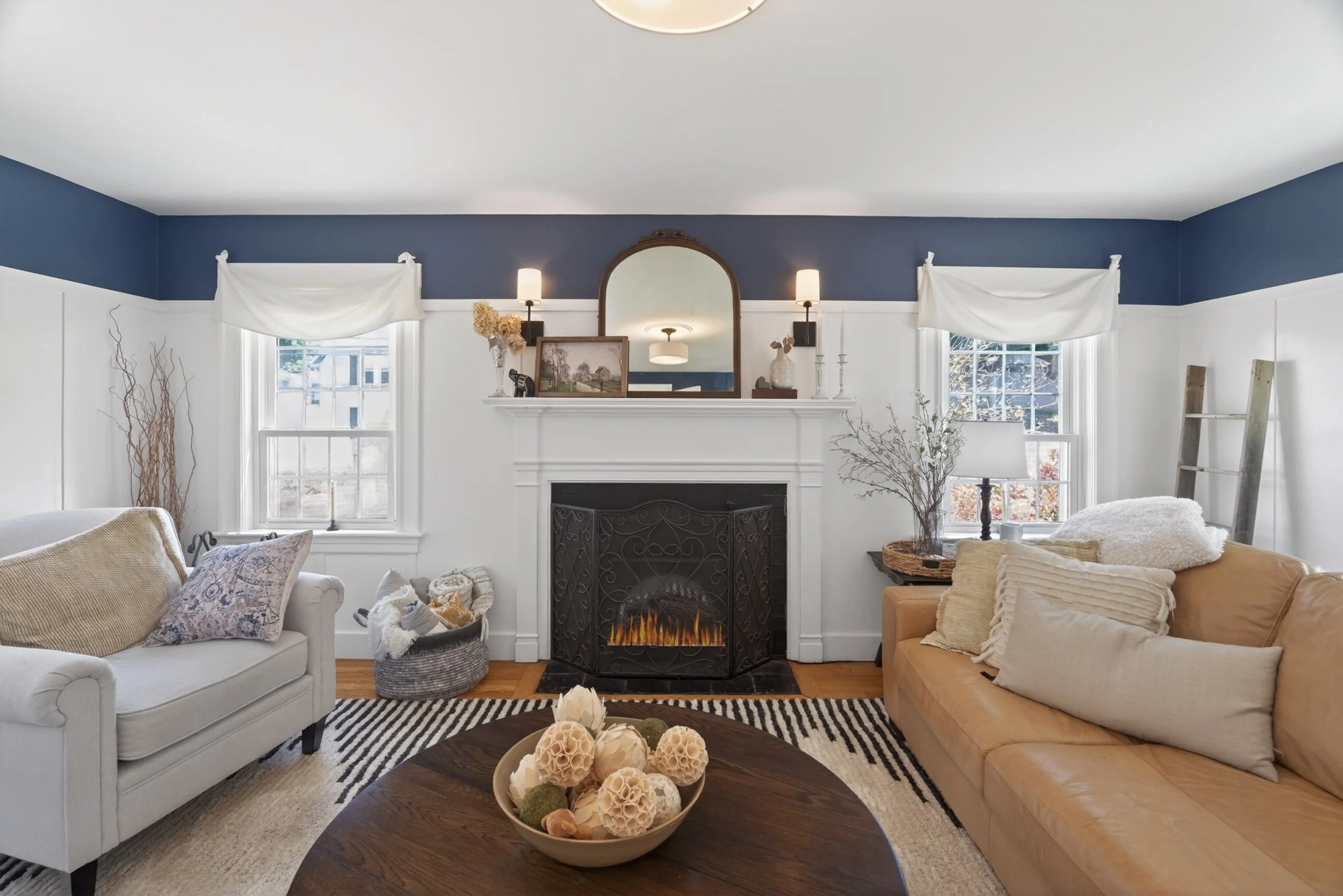 Living room with blue and white walls, a fireplace, two sofas, a coffee table with decorative balls, and windows with white drapes.