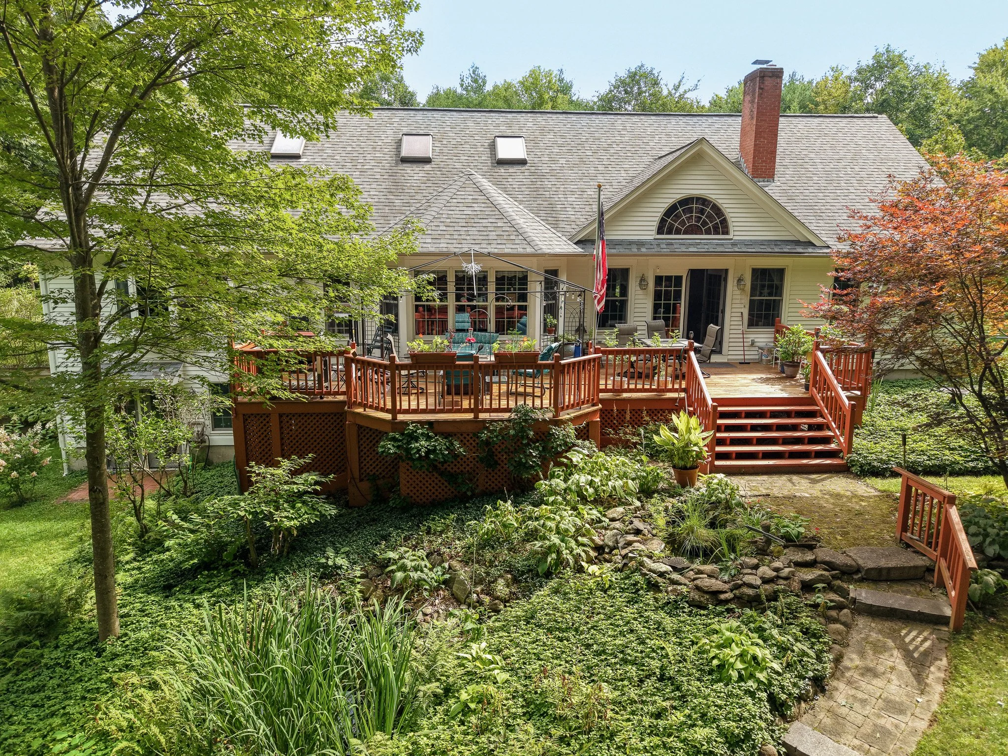 Backyard with wooden deck, patio furniture, American flag, trees, and lush green garden.