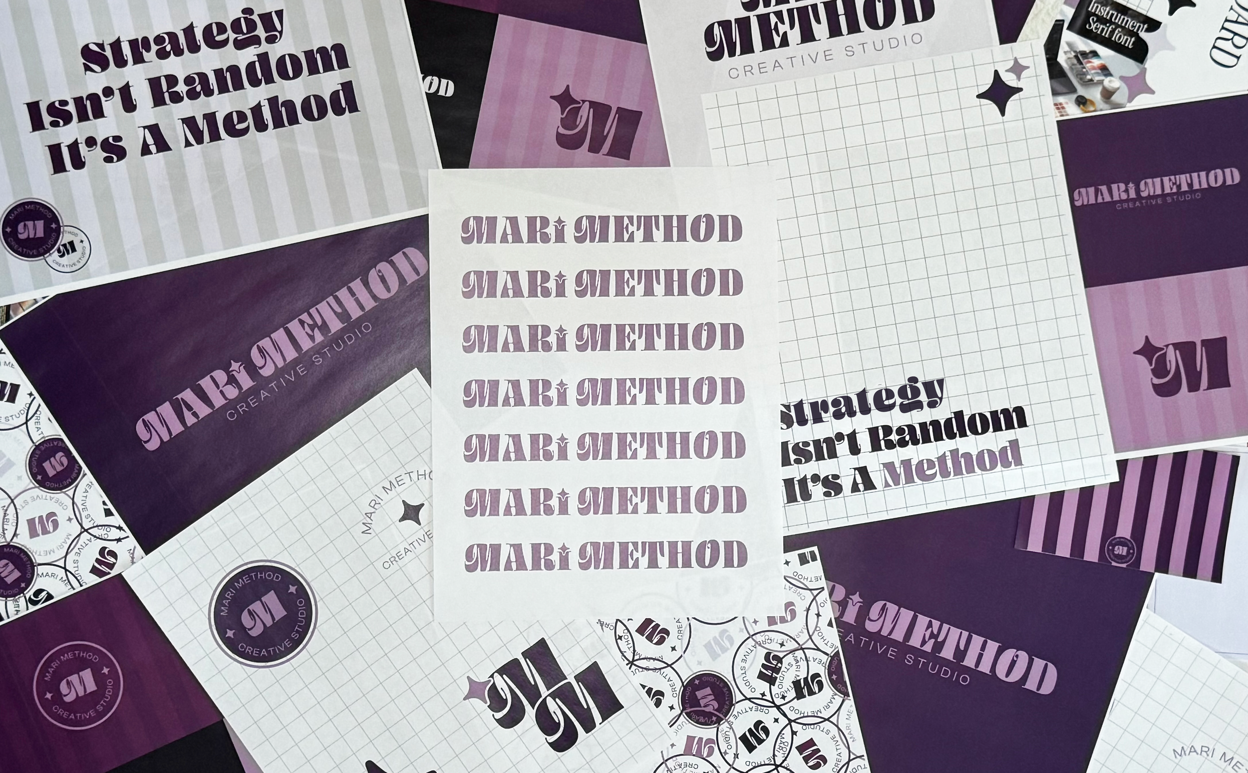 Various printed sheets and stickers with purple, black, and white designs related to 'Mari Method Creative Studio,' including logos, grid papers, and motivational phrases such as 'strategy isn't random, it's a method'.