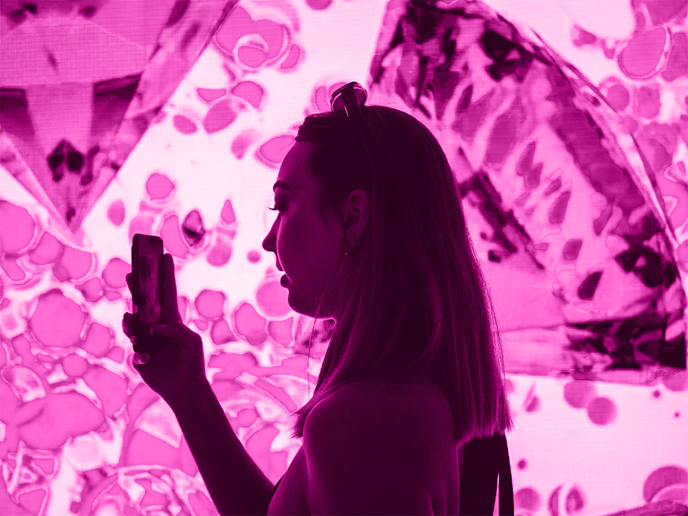 image of a young woman holding a phone up to an interactive art installation