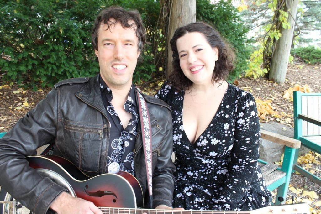 photo of a man and woman. the man is visually impaired and holding a guitar. the woman is wearing a dress.