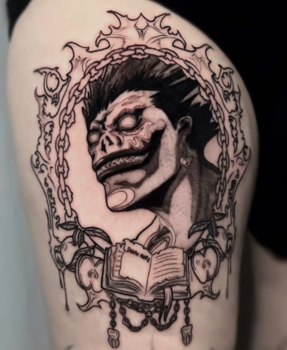 Tattoo of a clown's face with a sinister smile, surrounded by chains, an open book, and jewelry on the arm.