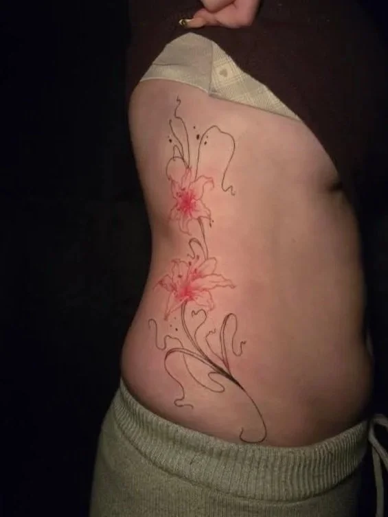 Side view of a person's torso with a floral tattoo design featuring lilies and decorative swirls.